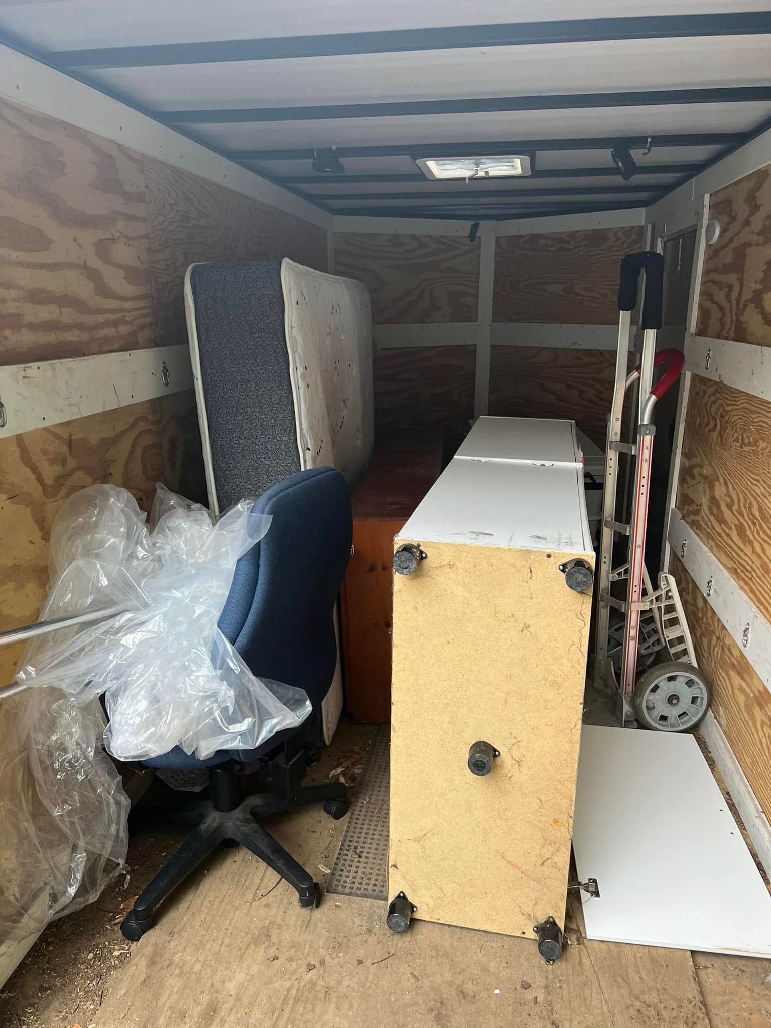 Packed moving truck interior with office furniture, a chair, bubble wrap, and flat-packed panels.