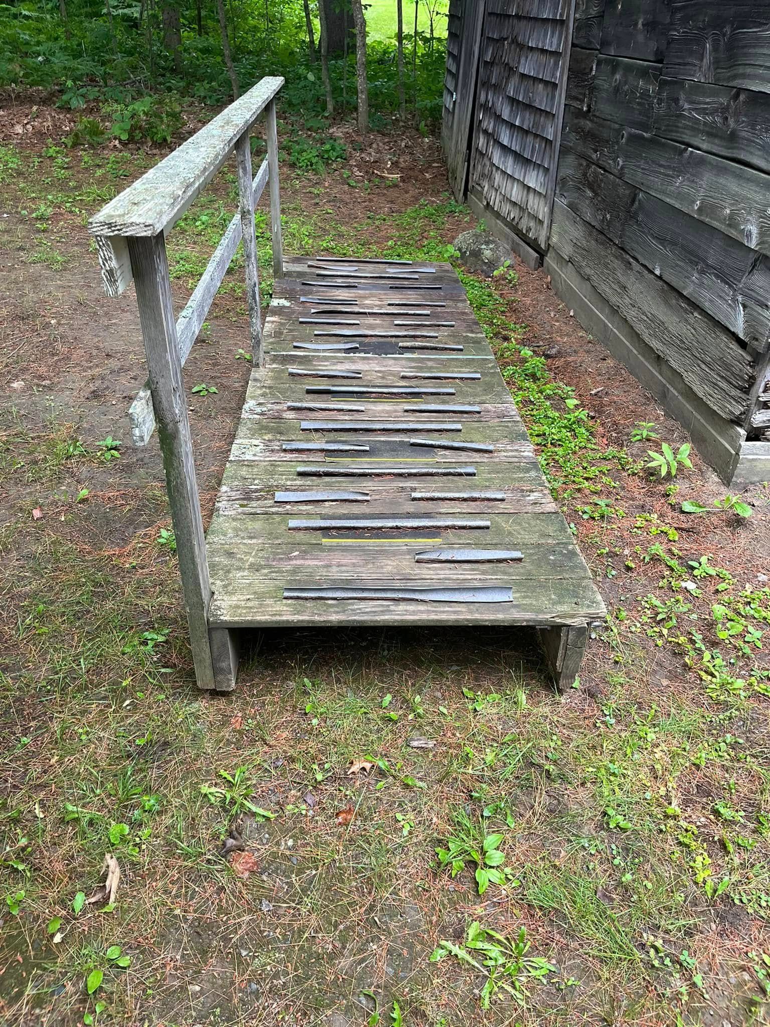 Narrow wooden footbridge over grass beside a weathered shed and fence.