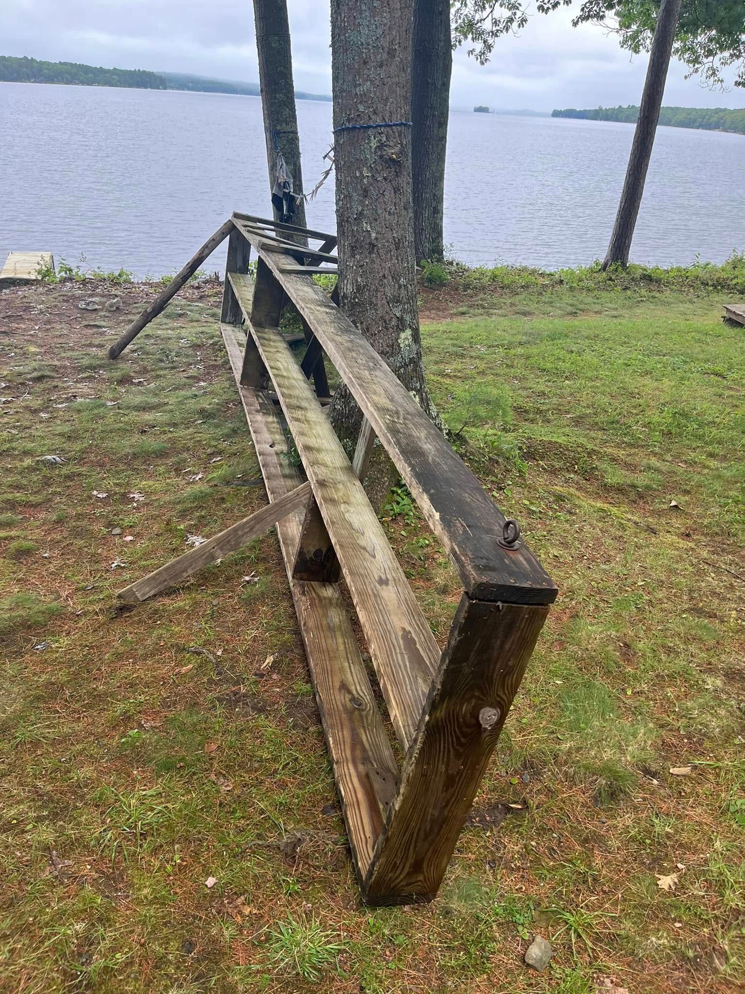 Broken wooden bench by a lakeside with a tree and grassy shore in the background