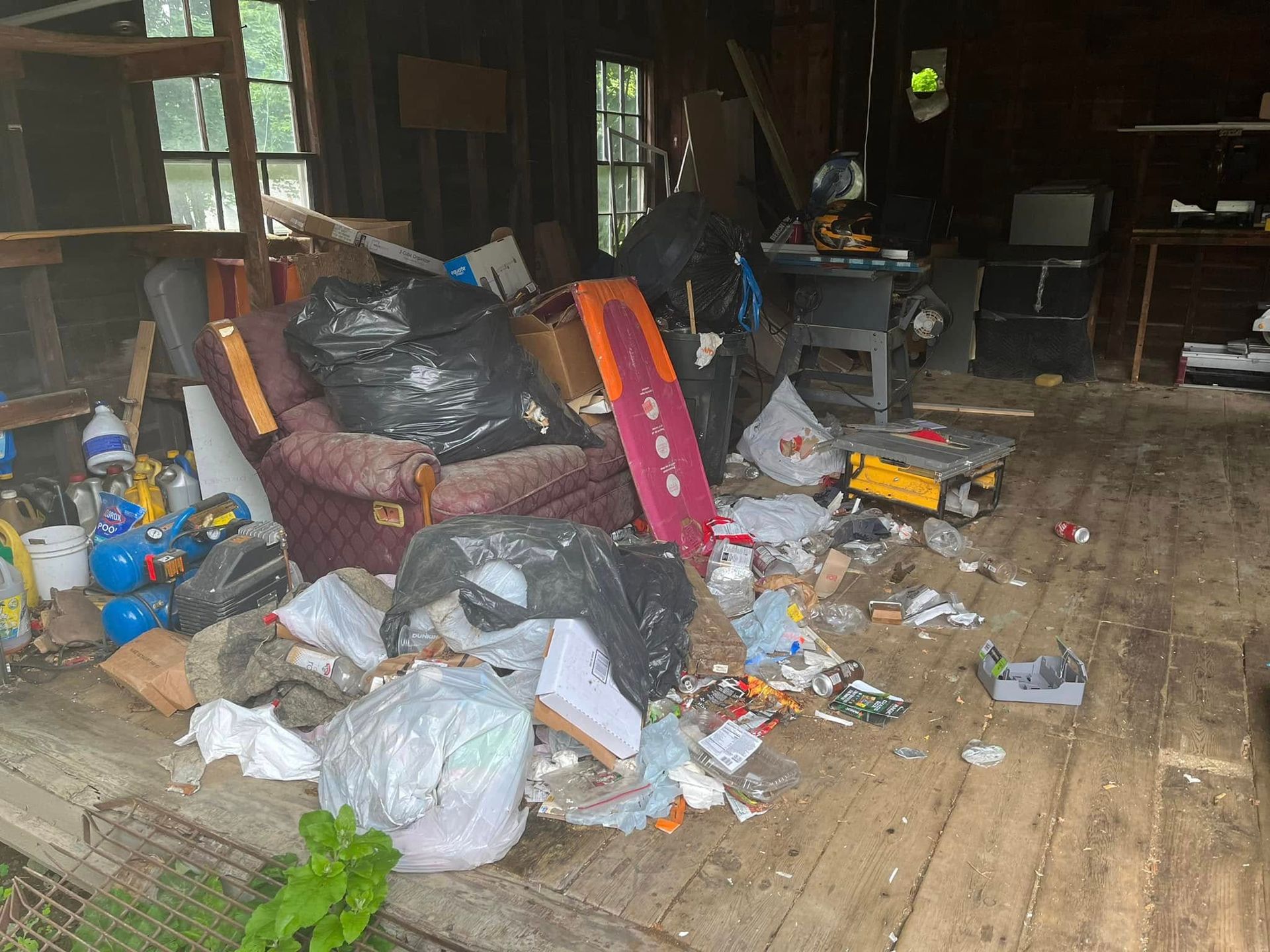 Cluttered room with piles of trash bags, bottles, and debris scattered across the floor and furniture.