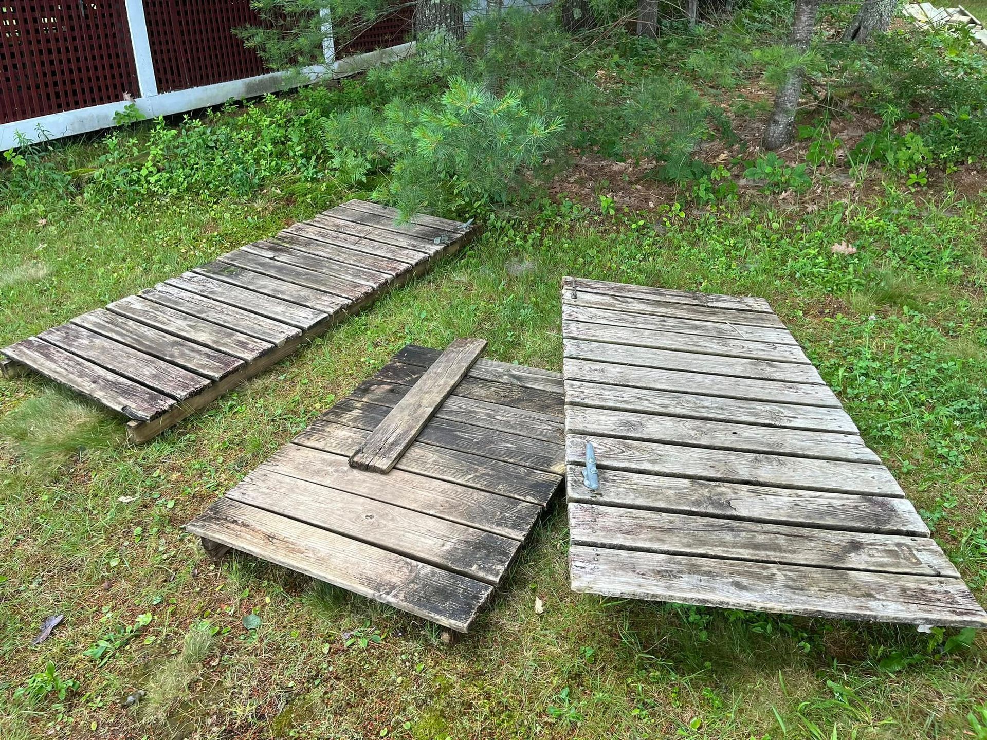 Three weathered wooden ramps or planks lying on grass near a fence.