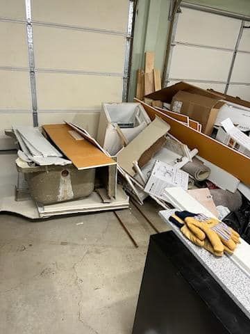 Cluttered garage floor with broken cardboard boxes and scattered packing debris near a workbench.