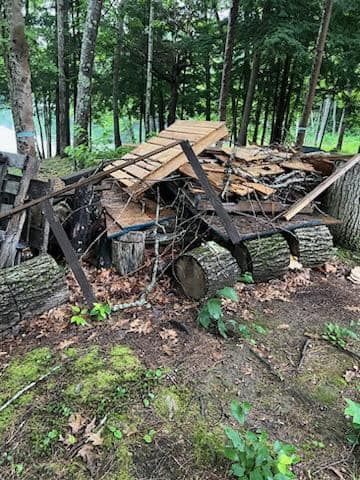 Collapsed wooden shed in a wooded area, with broken boards and debris on the ground