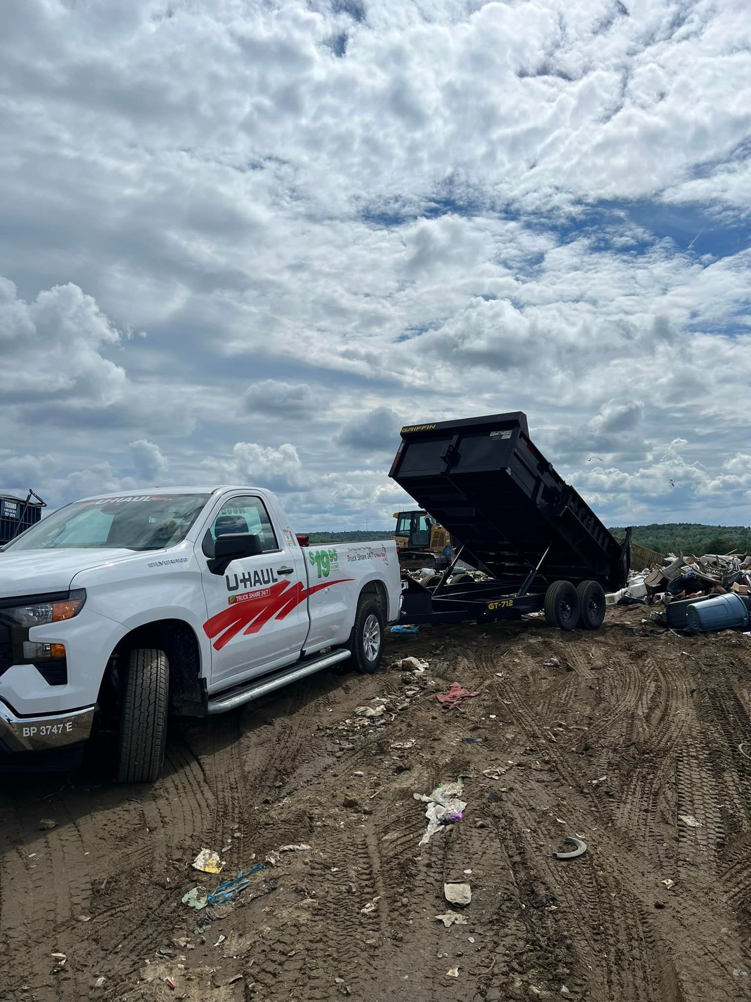 White tow truck and a black dump truck on a muddy road under a cloudy sky