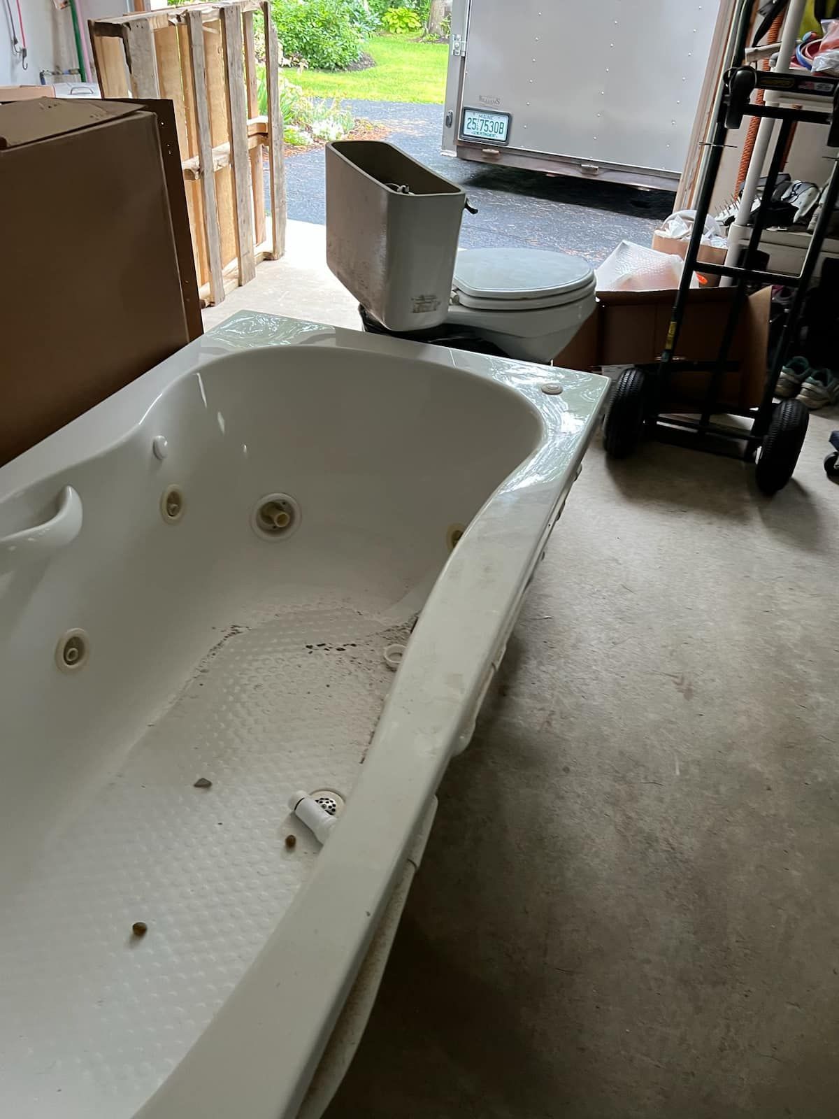 Bathtub in a cluttered room with tools and boxes, near an open doorway to outside.