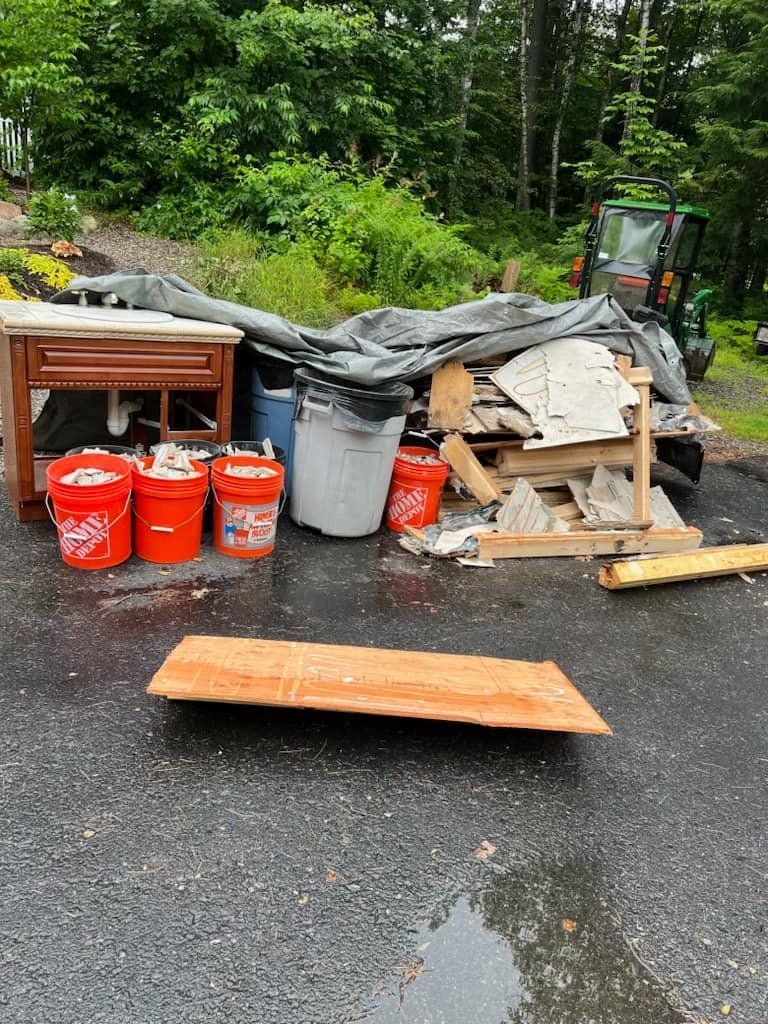 Storm-damaged debris piled on asphalt beside trees, with red gas cans and broken wood covered by tarp.