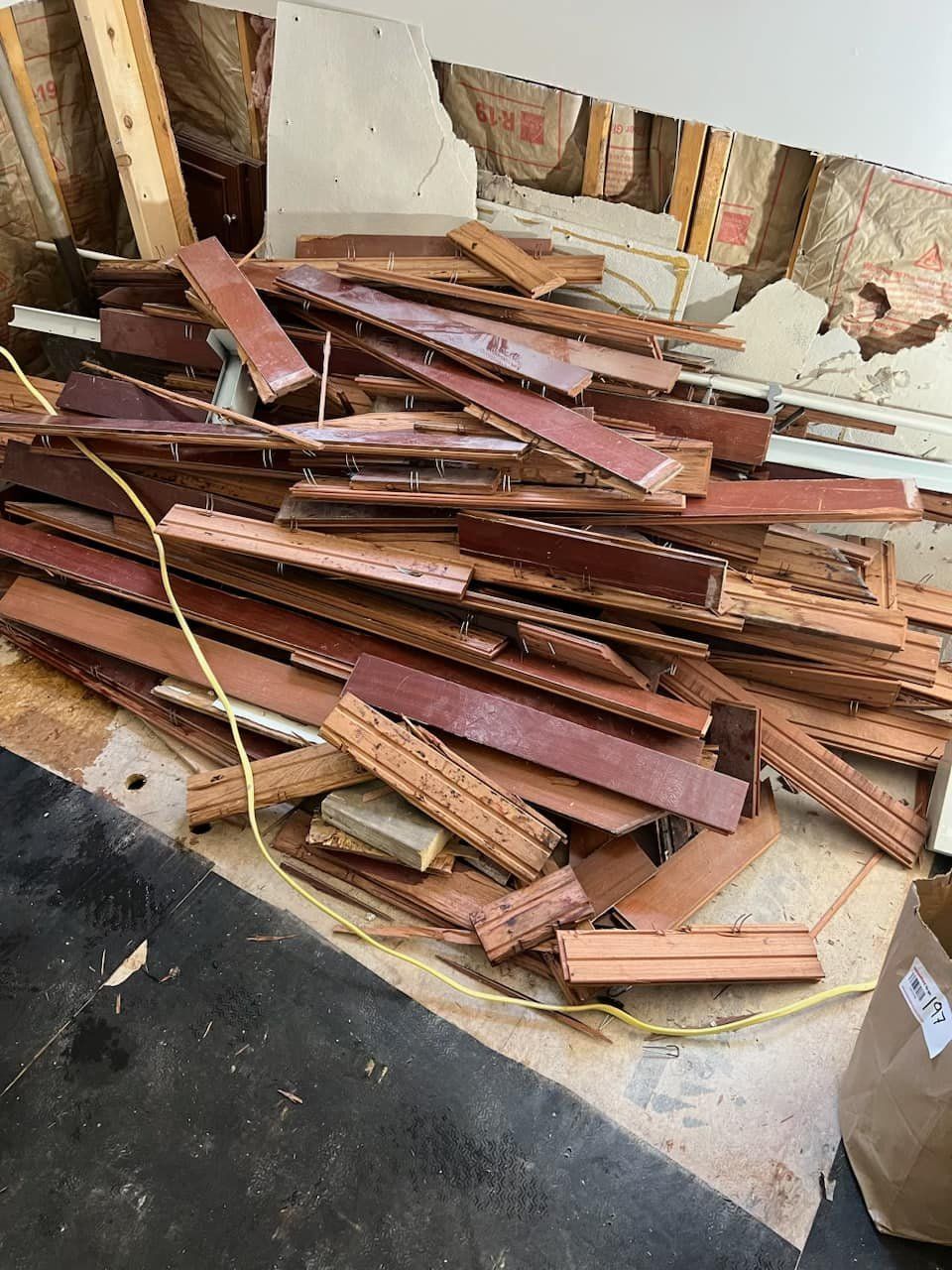 Pile of reddish-brown wood scraps and molding piled on a floor in a damaged room.