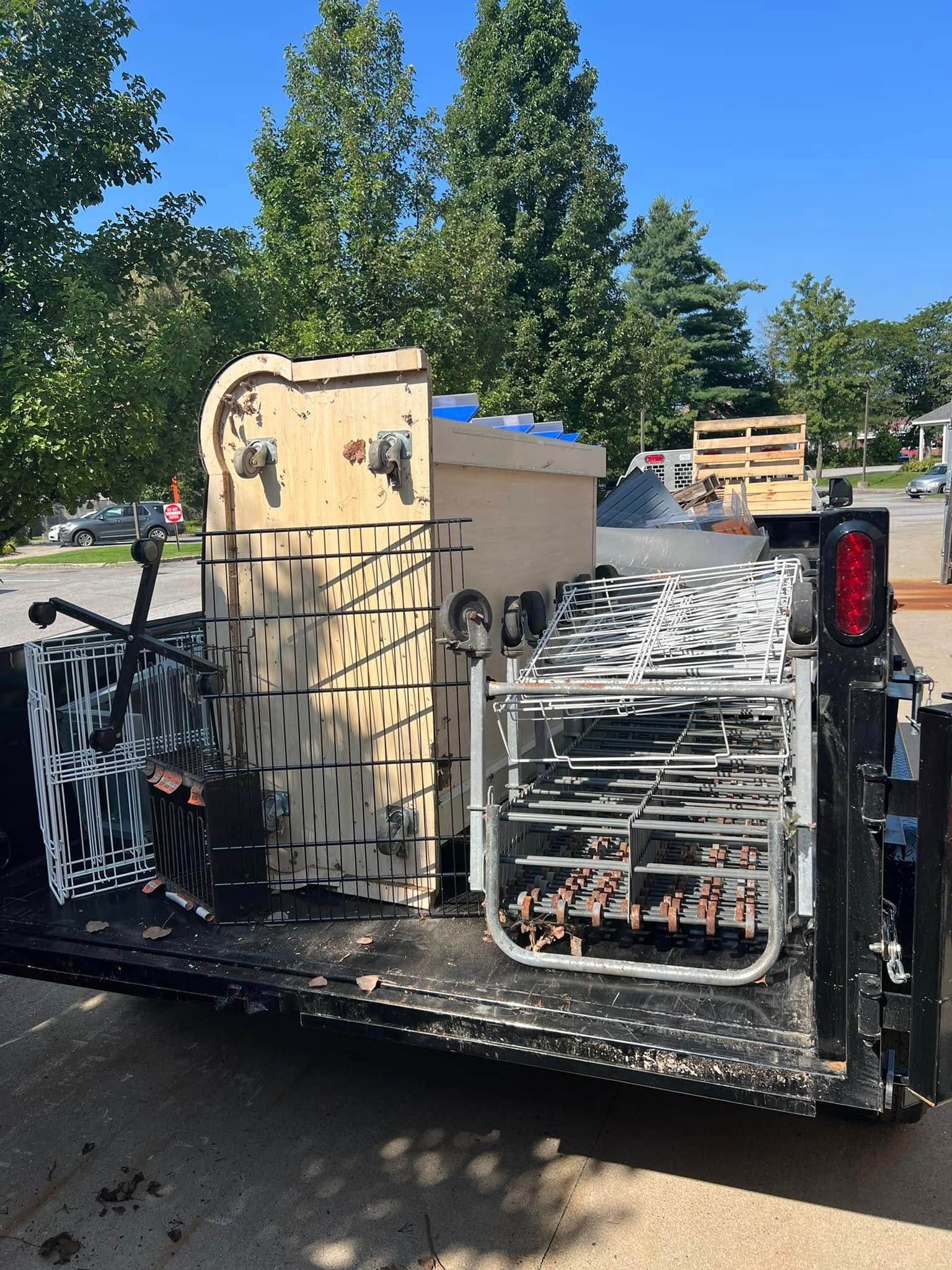 Trailer loaded with stacked metal carts and a wooden crate outdoors beside trees