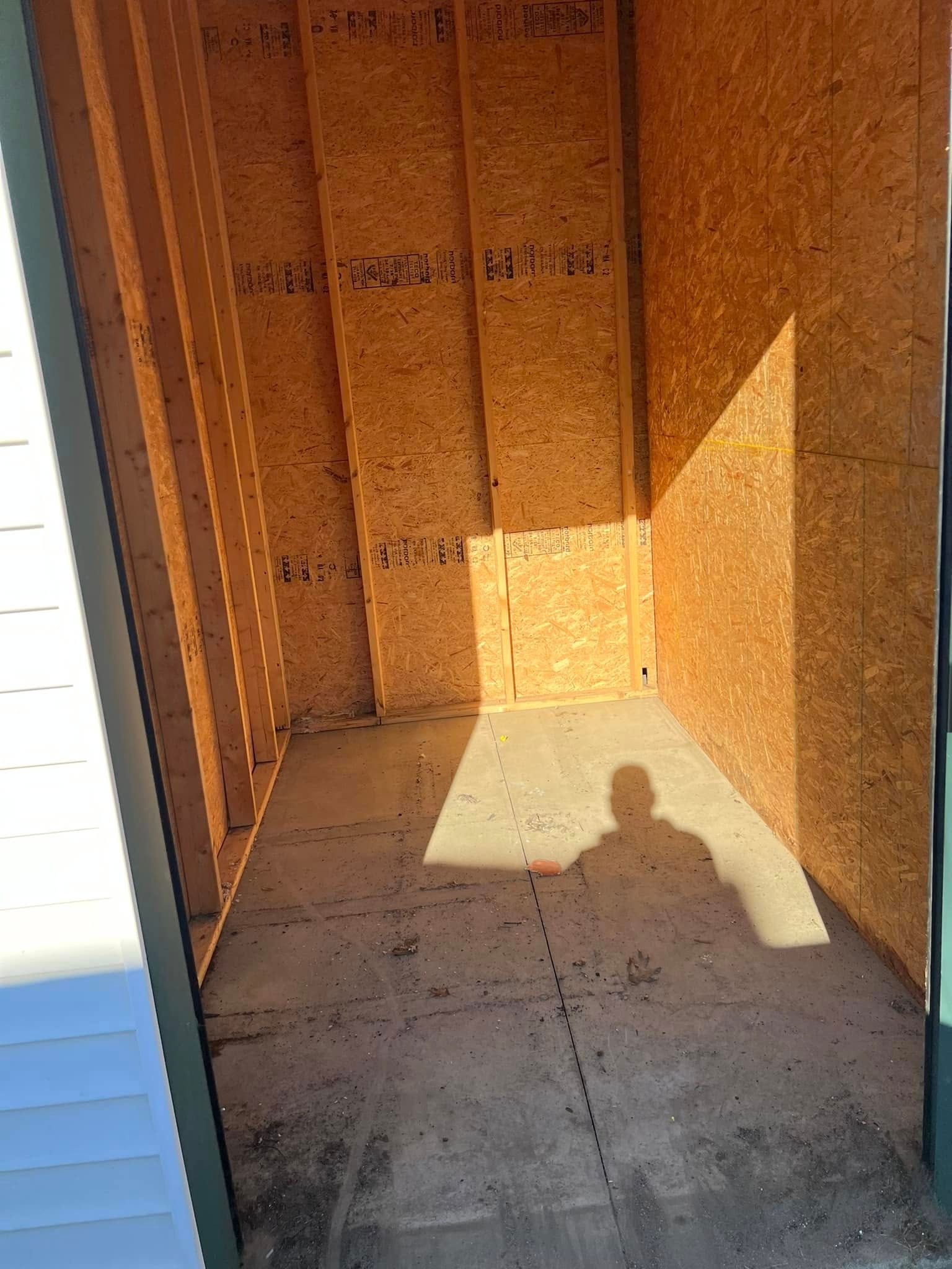 Empty wooden storage shed with sunlight on the floor and a shadow in the doorway.