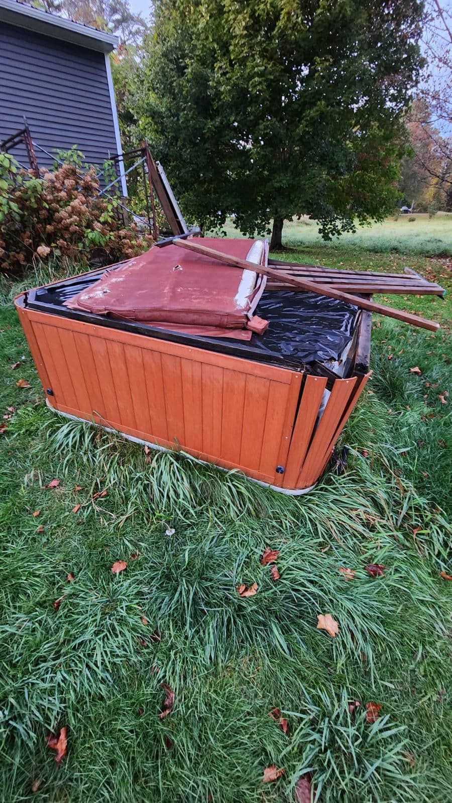 Broken orange hot tub tipped on its side in a grassy yard, with debris and a damaged cover.