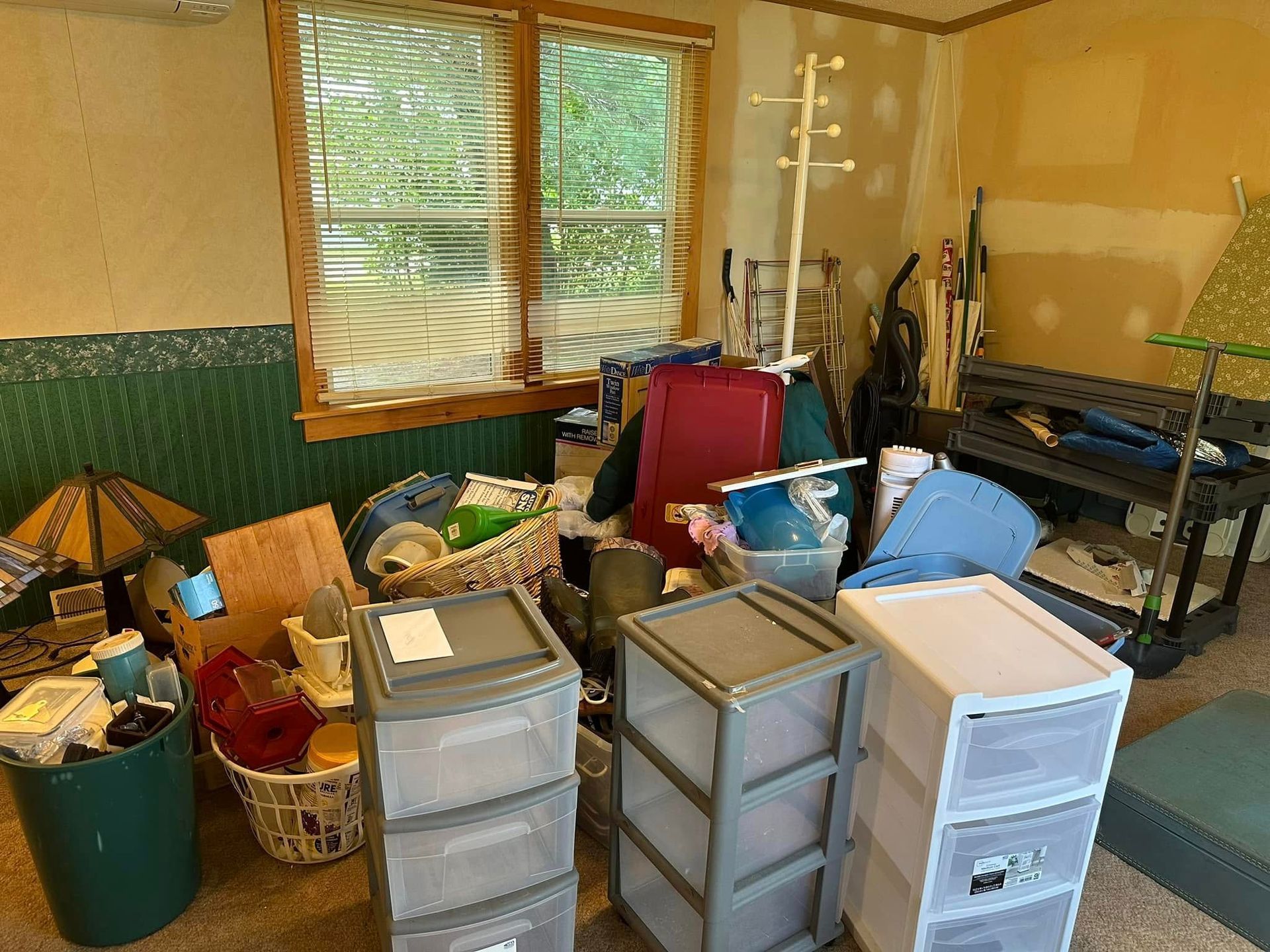 Cluttered room with plastic storage drawers, baskets, and tools beneath a window and shelves