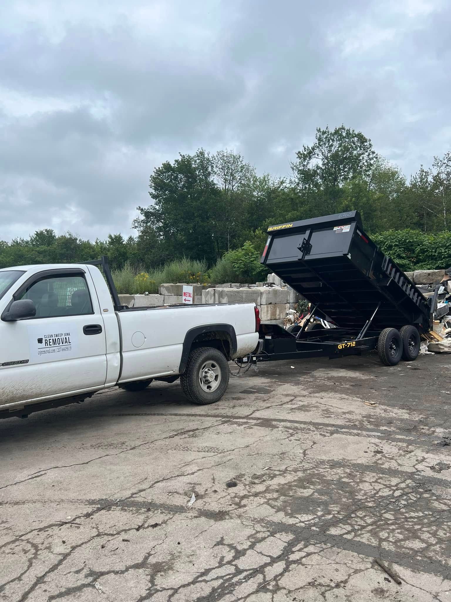White pickup truck with a raised dump trailer on cracked pavement under cloudy skies