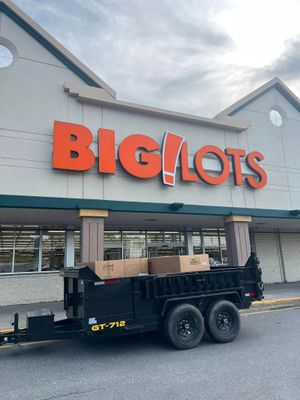 Black utility trailer with cardboard boxes parked outside a Big Lots store entrance