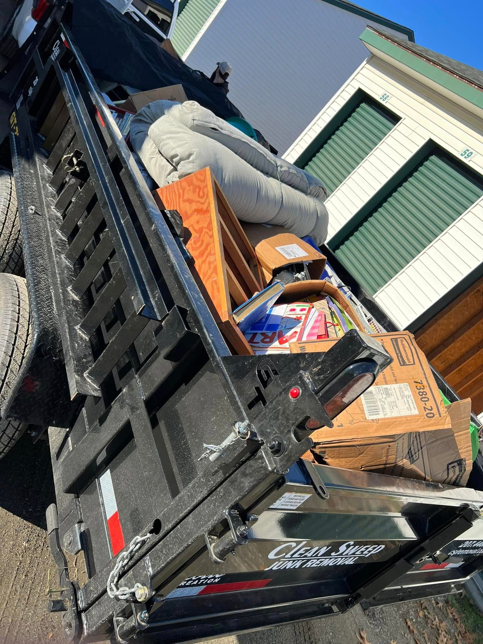 Trash bins and cardboard boxes piled in a black dumpster beside a brick building and parked truck.