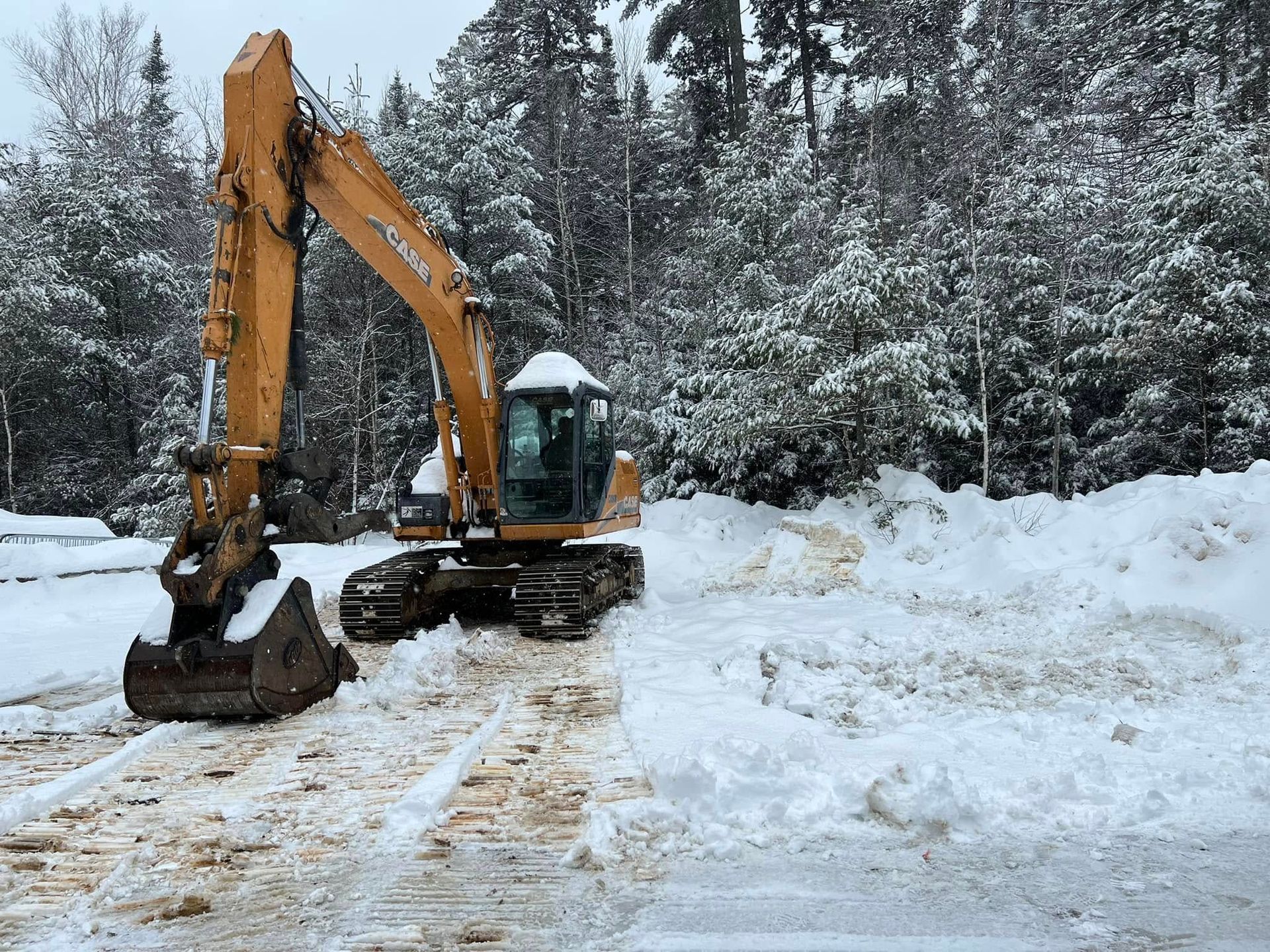 Yellow excavator clearing snow on a snowy forest road