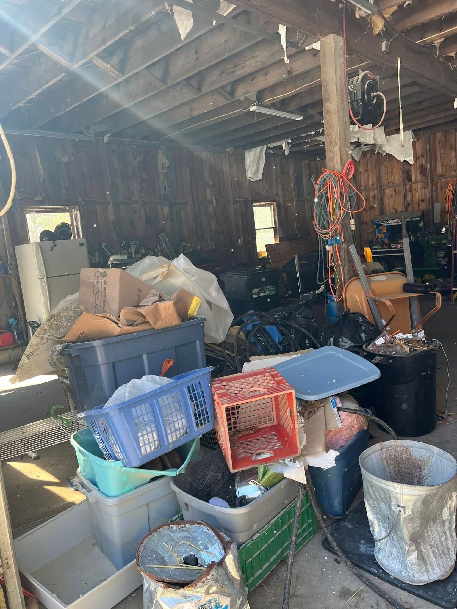 Cluttered shed interior with boxes, bins, tools, and hanging items under a wooden roof