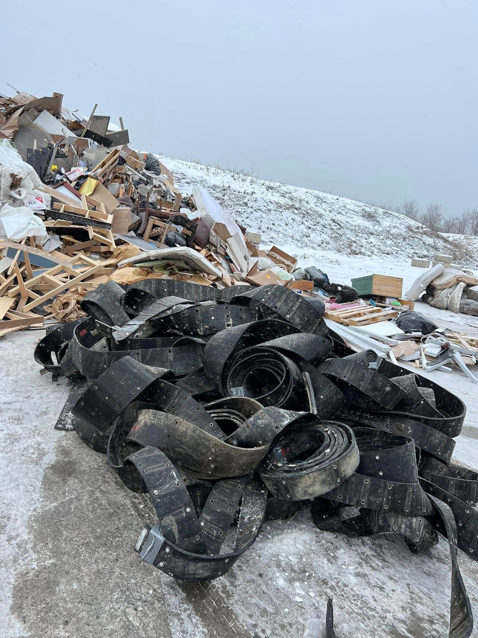 Piles of black tires and mixed debris on a snowy roadside under a gray sky