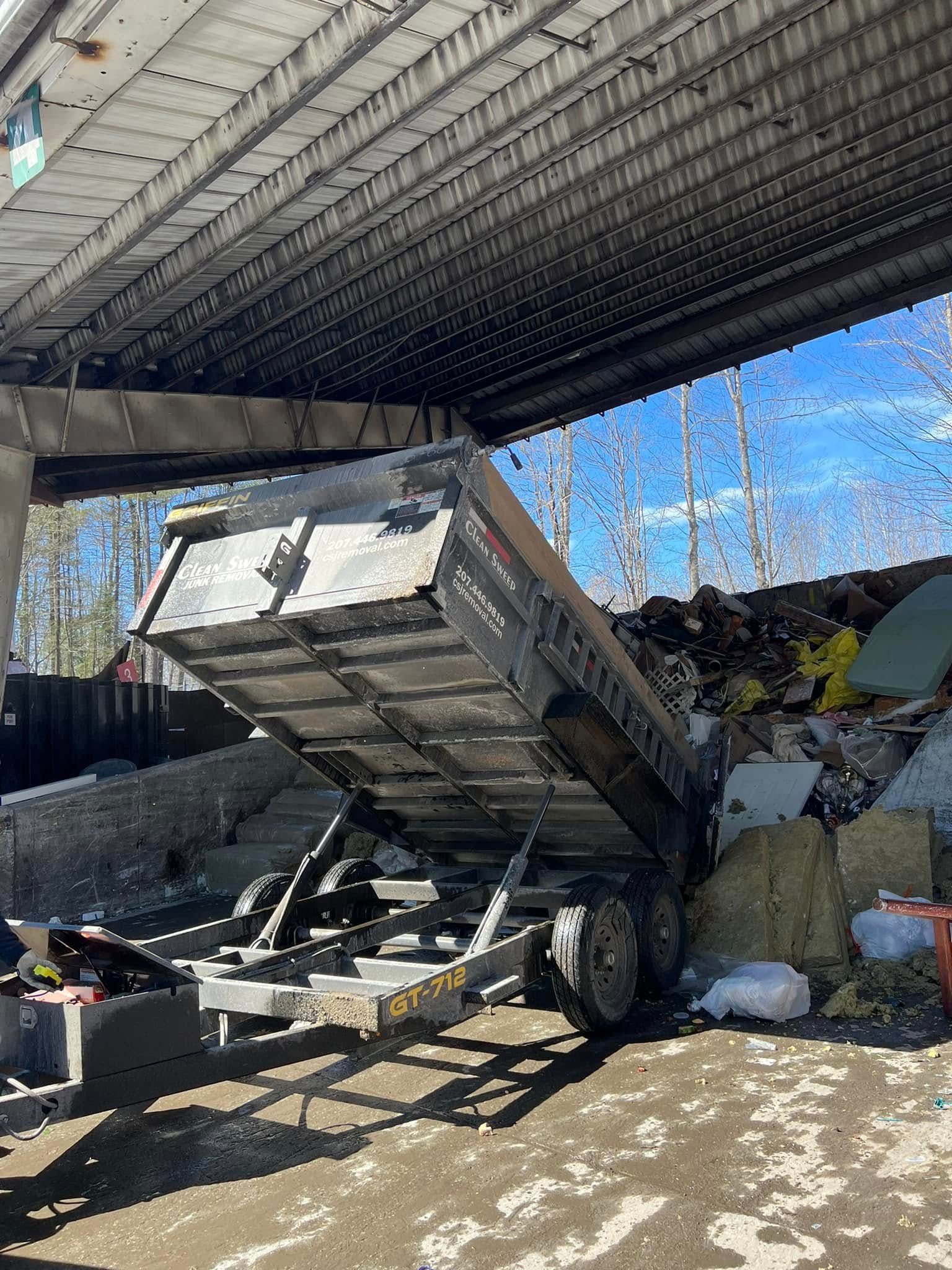 A tipped dump truck under a bridge beside rubble and muddy ground on a sunny day