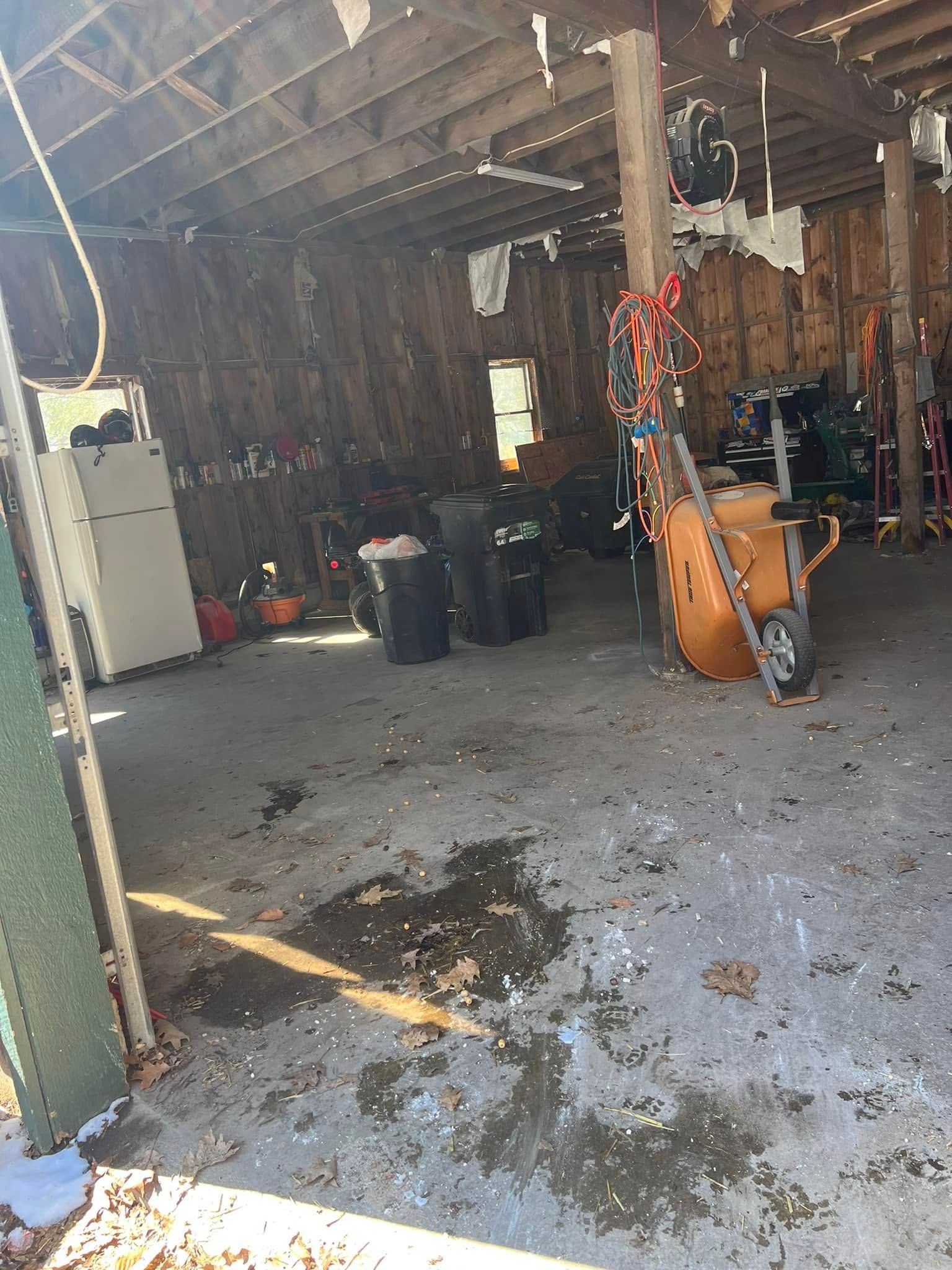Messy garage with wet concrete floor, trash bins, tools, and an orange bicycle leaning against a post