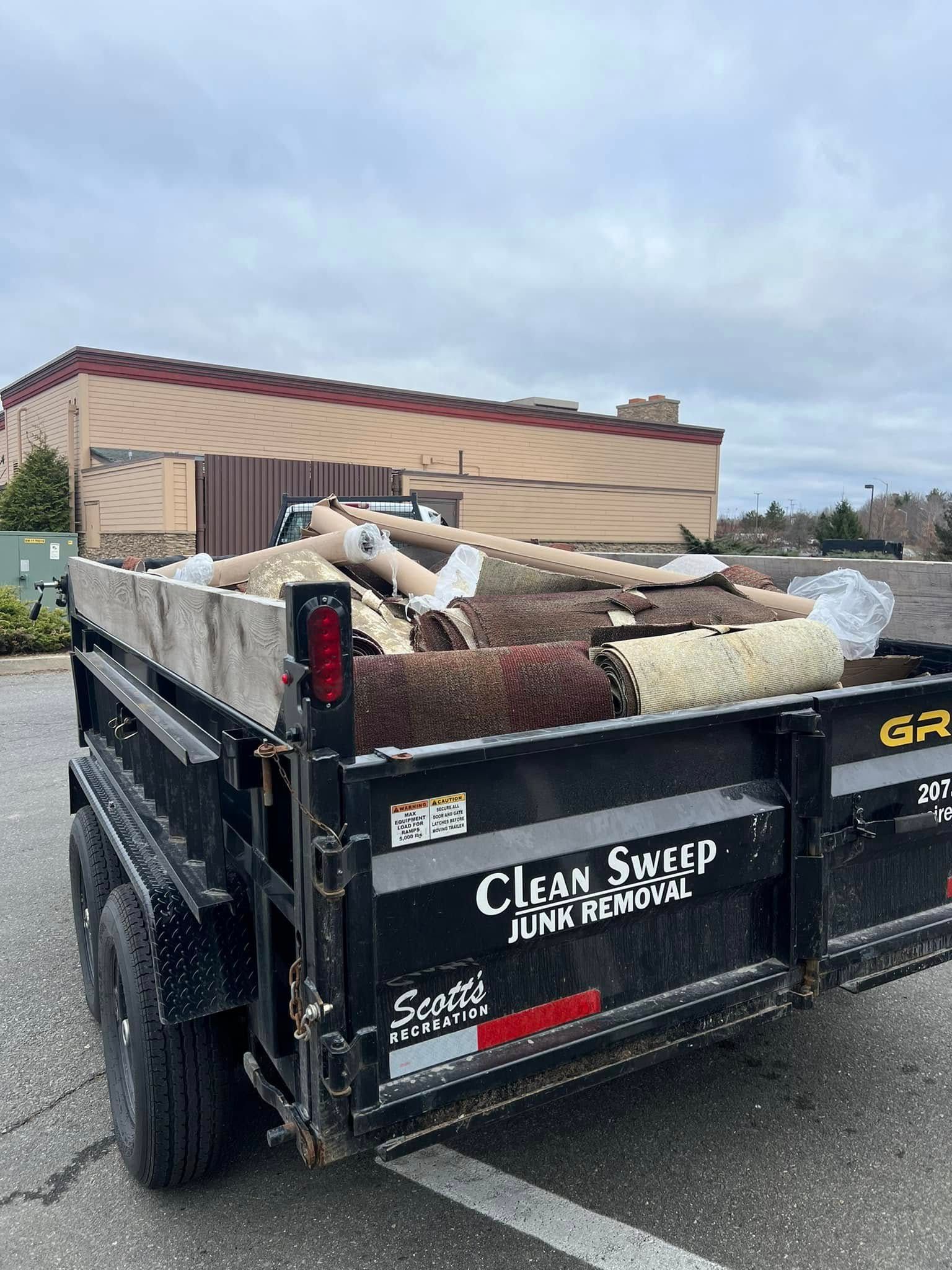 Black dump trailer loaded with yard debris in a parking lot outside a tan building