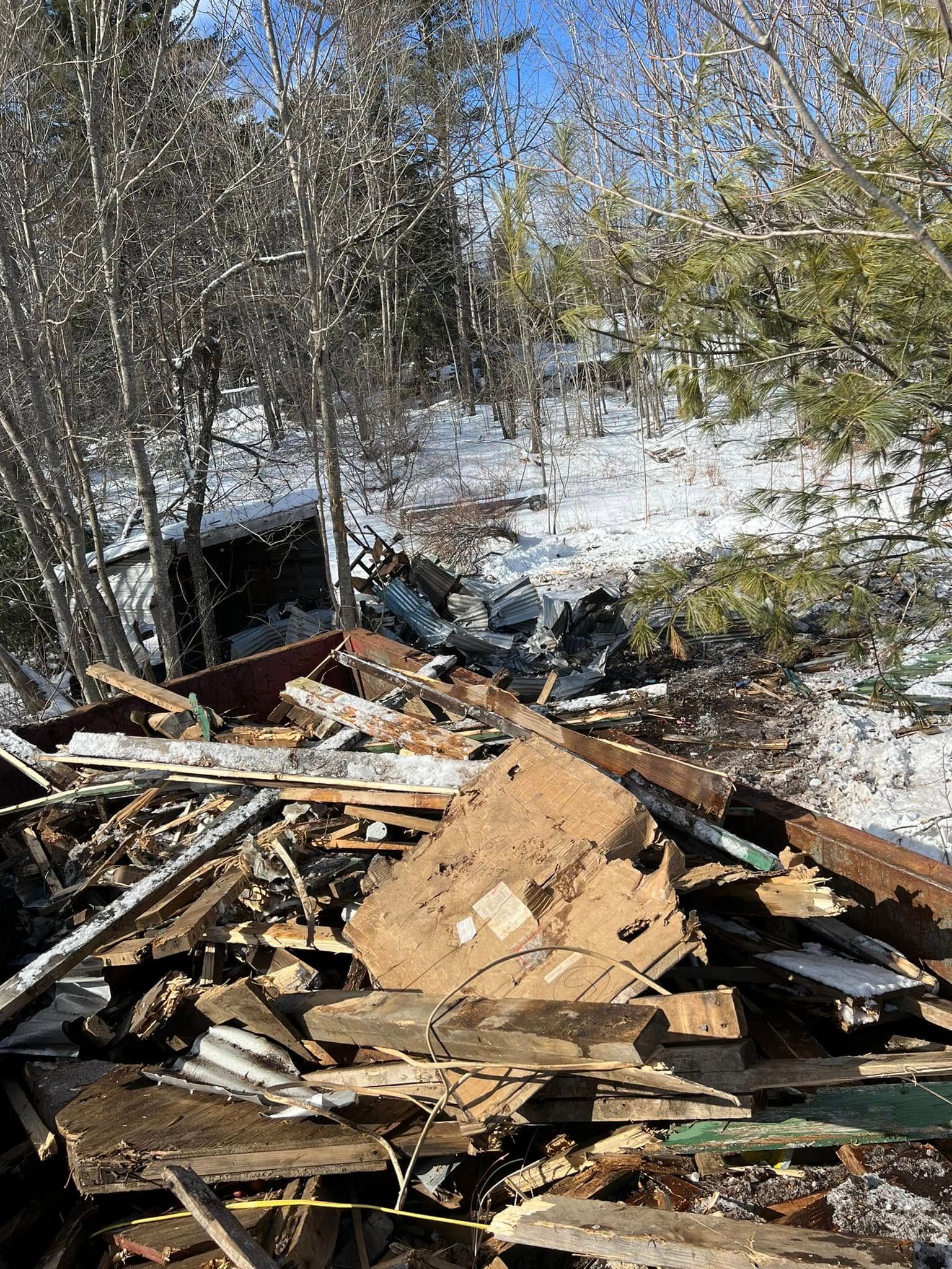 Pile of broken wood and debris in a snowy outdoor area with leafless trees