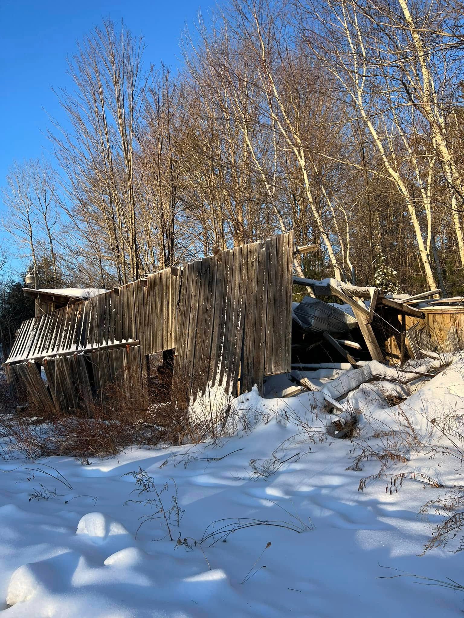 Snow-covered yard with a weathered wooden fence and leafless trees under a clear blue sky