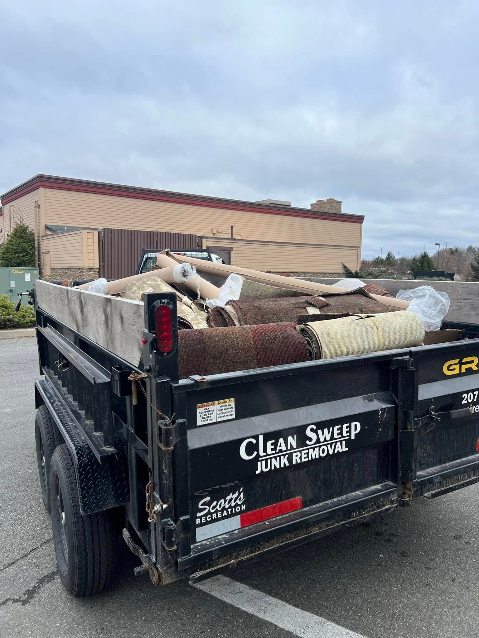 Black dump trailer loaded with debris in a parking lot near a tan building
