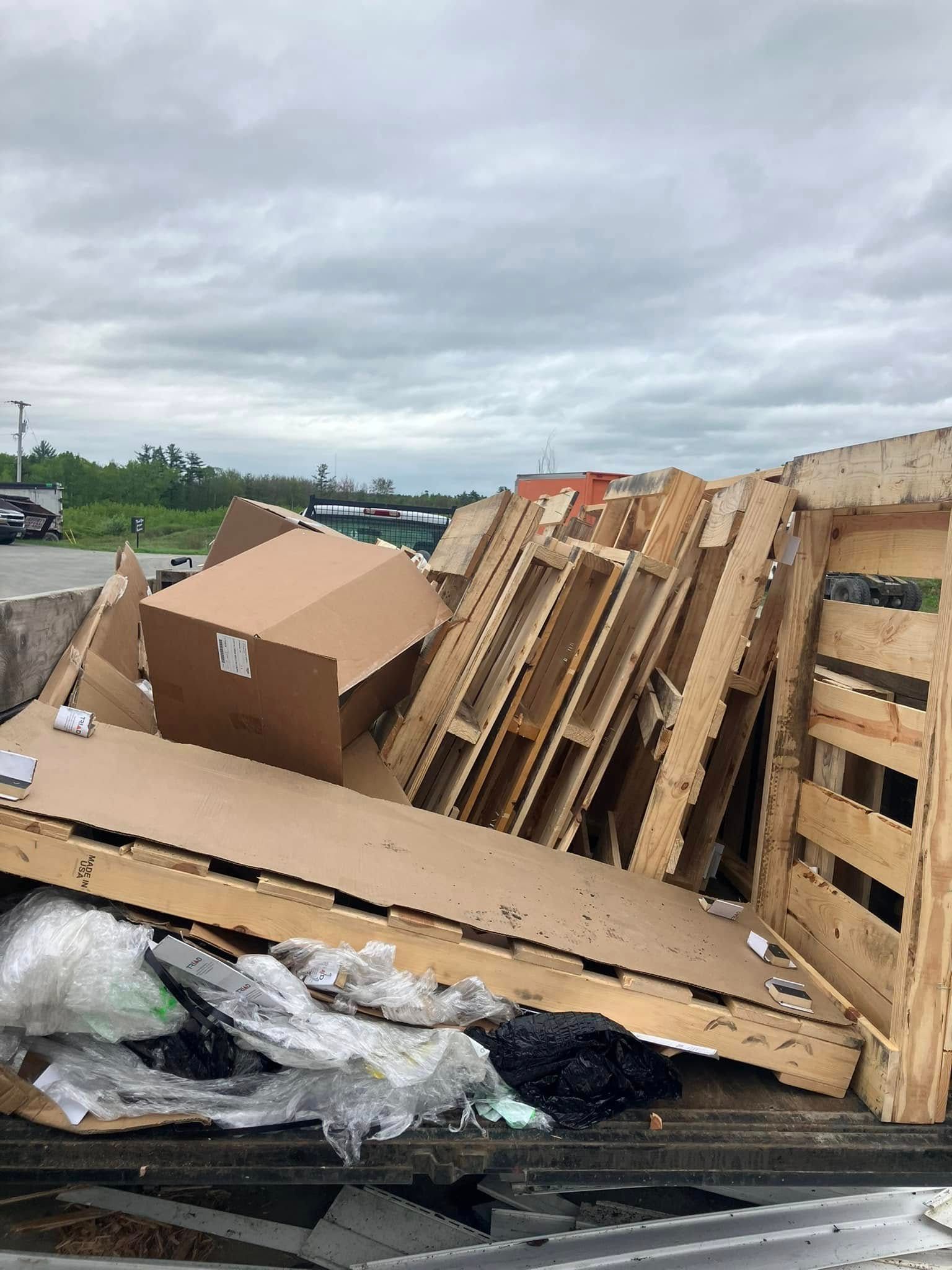 Pallets and cardboard debris piled in a landfill under a cloudy sky.