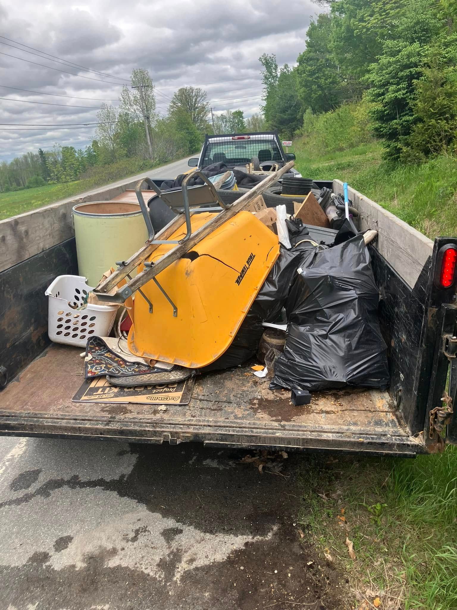 Debris and broken orange equipment piled in a trailer beside a roadside ditch under cloudy skies