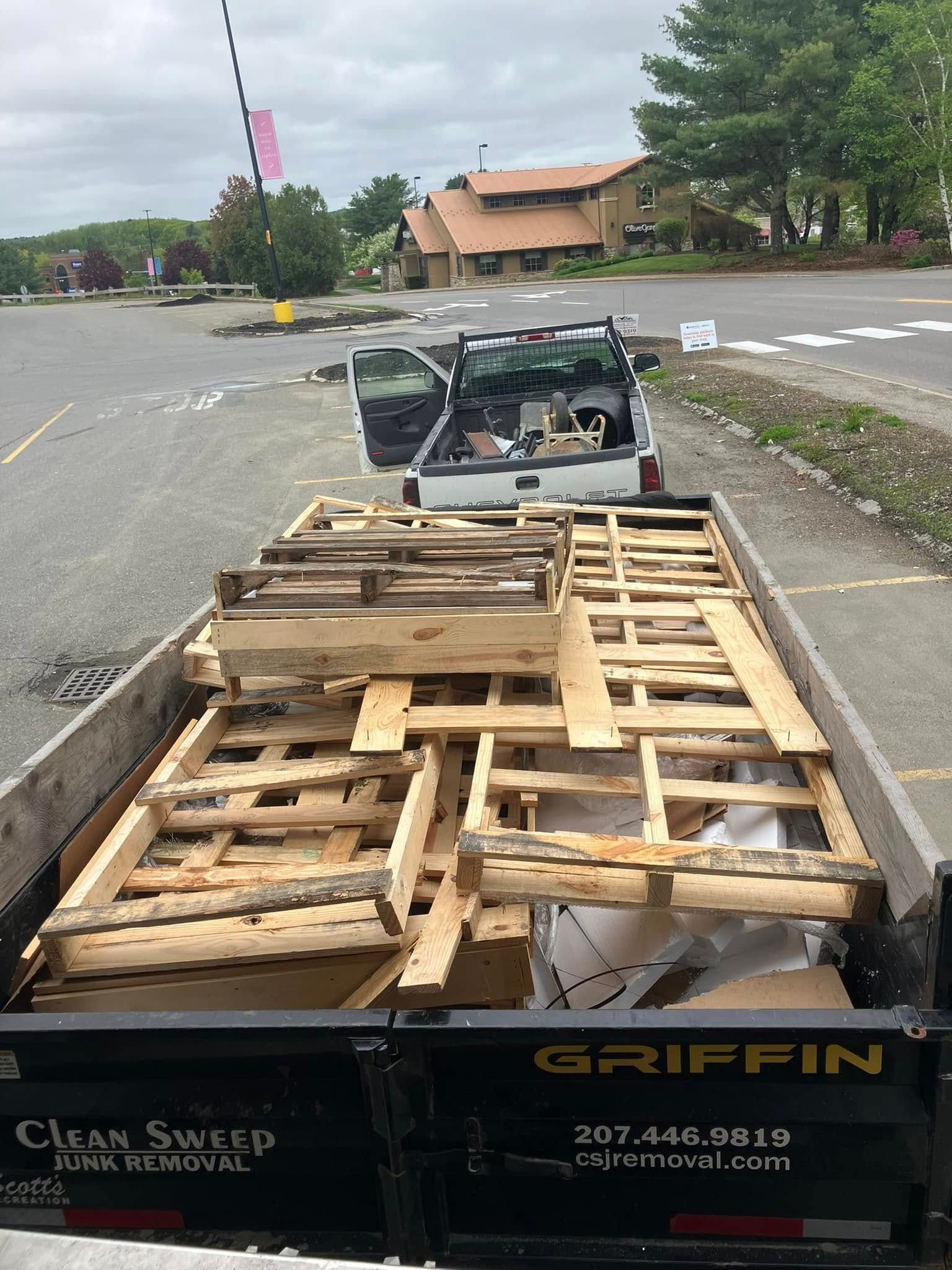 Truck bed loaded with wooden pallets at a road construction site, with a utility cart ahead.