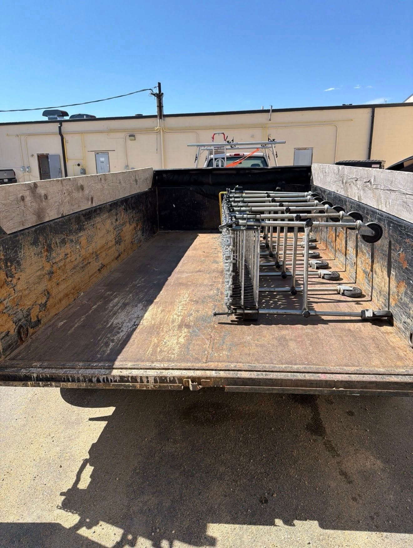 Flatbed trailer loaded with metal racks and equipment in a sunny industrial yard.