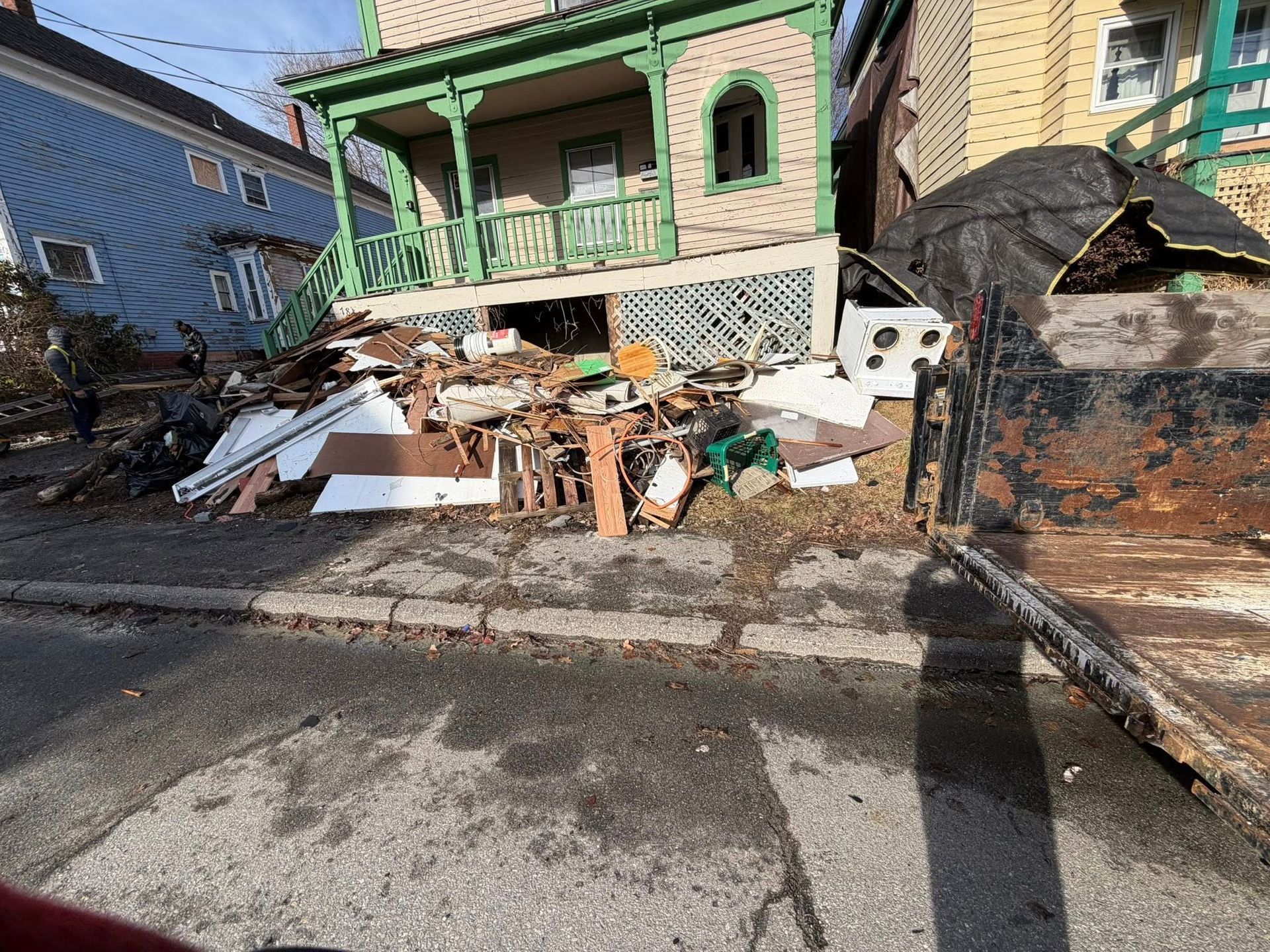 Collapsed porch and debris pile in front of a yellow house after storm damage