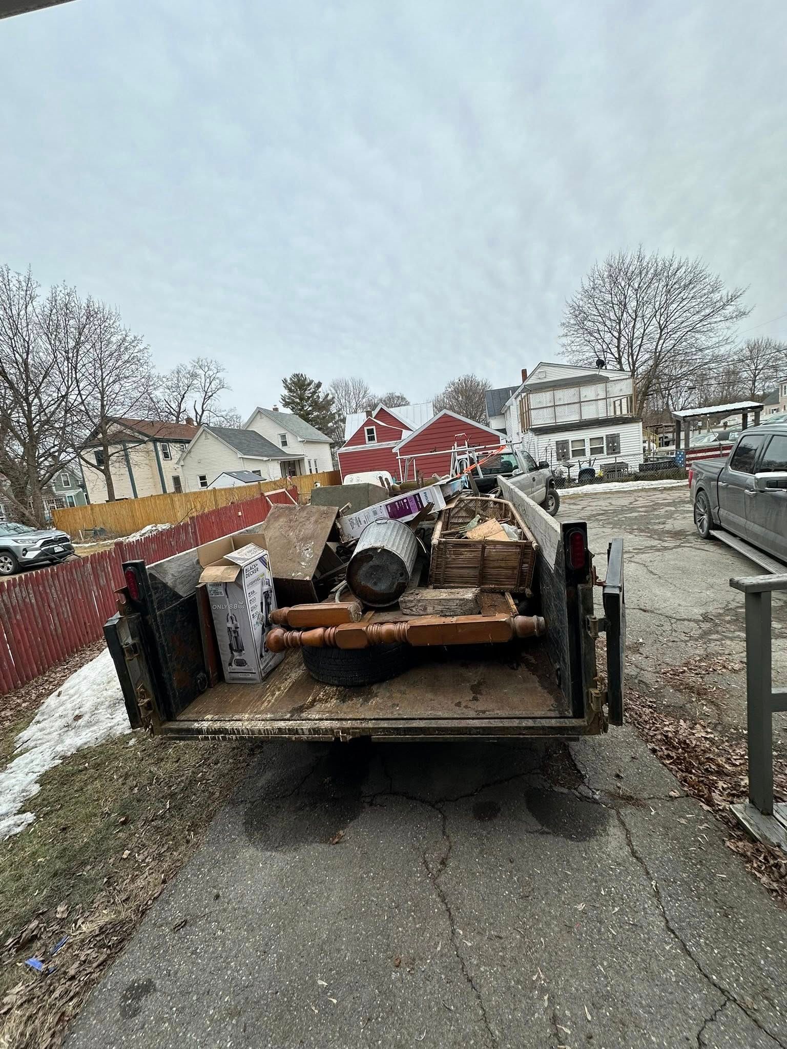 Flatbed trailer loaded with debris and wood on a residential street, with snow on the ground.