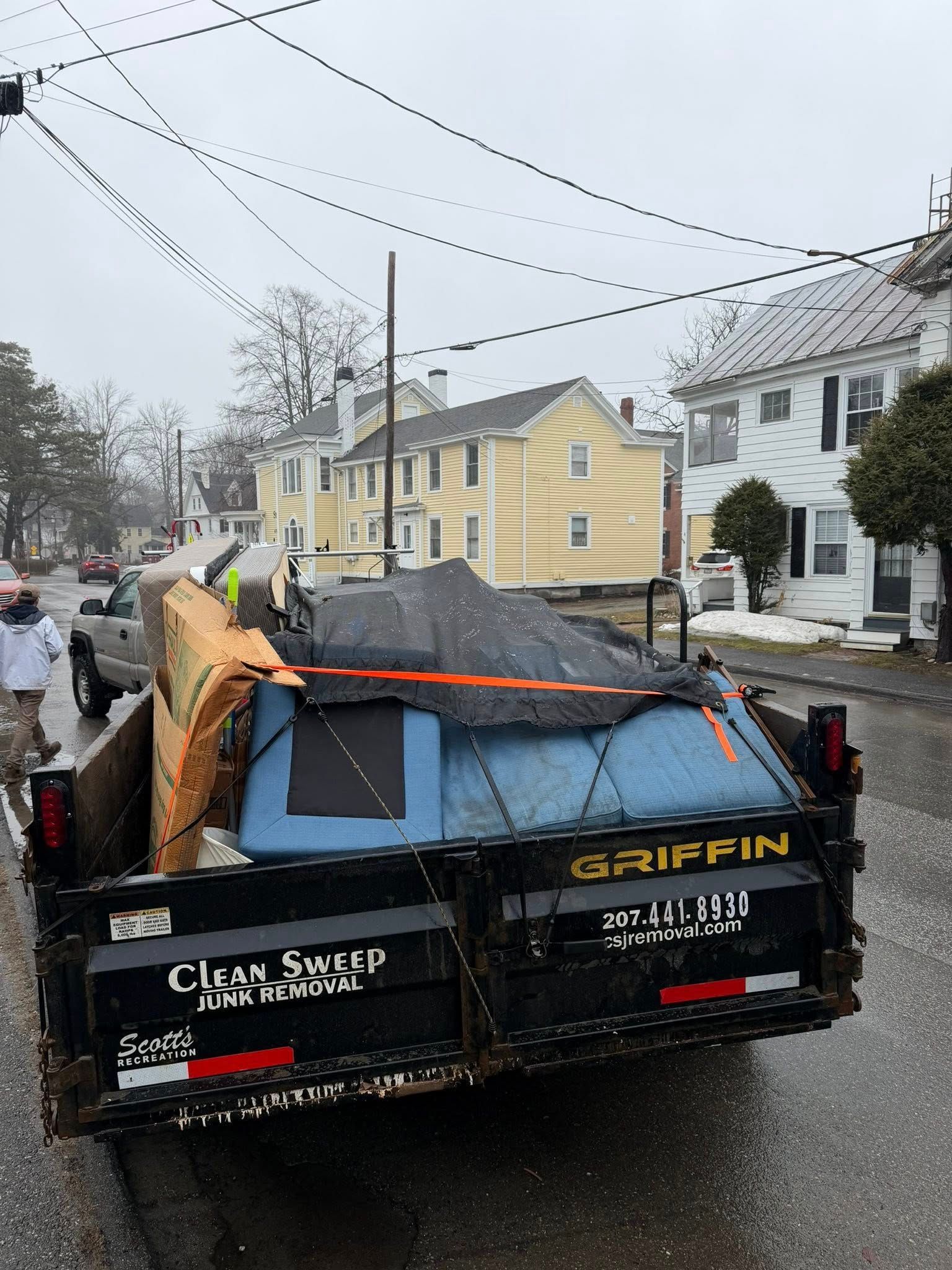 Damaged Griffin dumpster truck on a wet residential street after storm, with debris piled in back