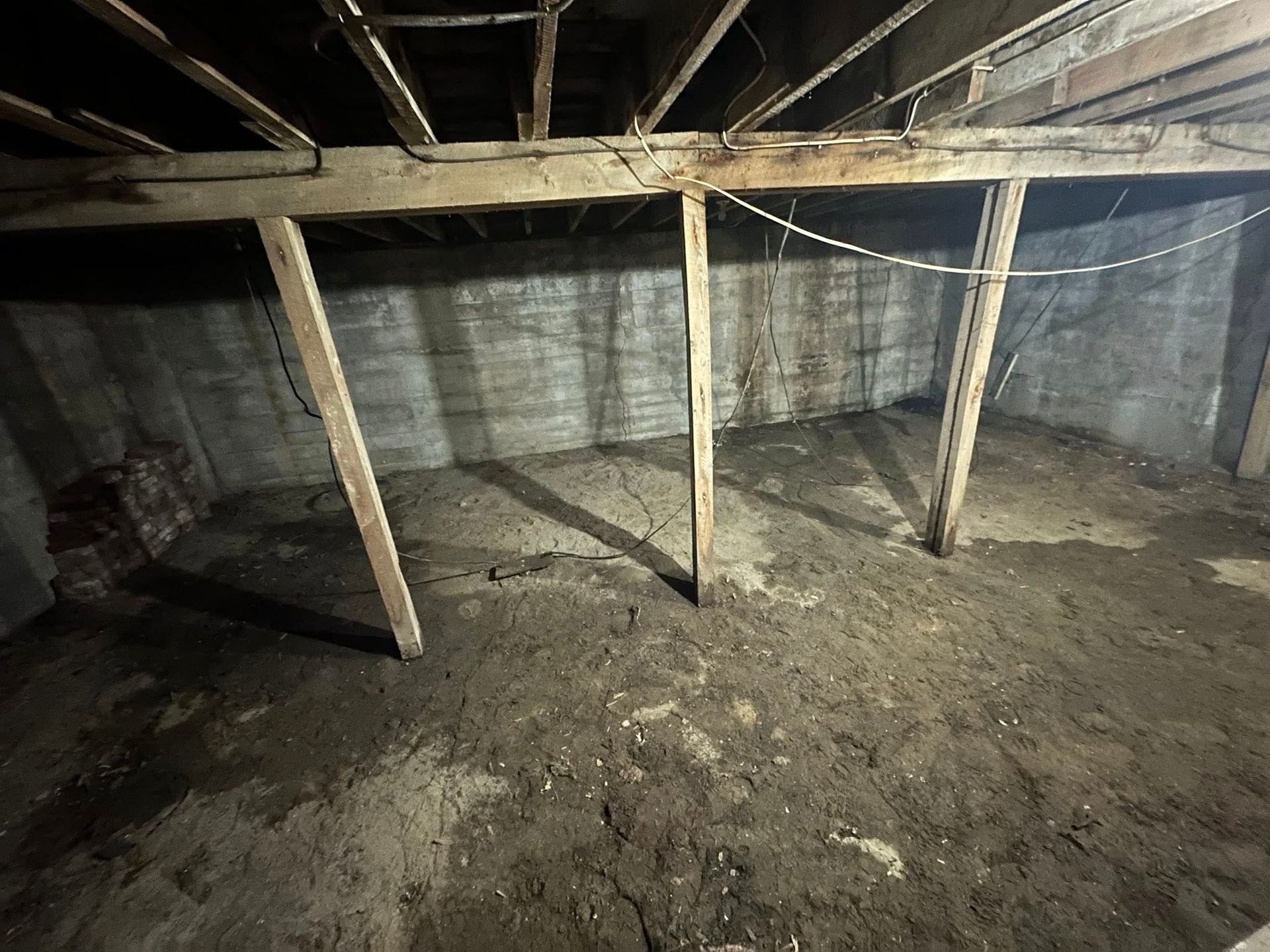 Dusty crawl space with exposed wooden beams and concrete walls supported by vertical posts