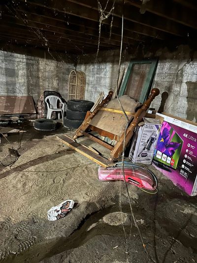 Flooded basement with debris, a tipped wooden chair, stacked tires, and a colorful board leaning against the wall.