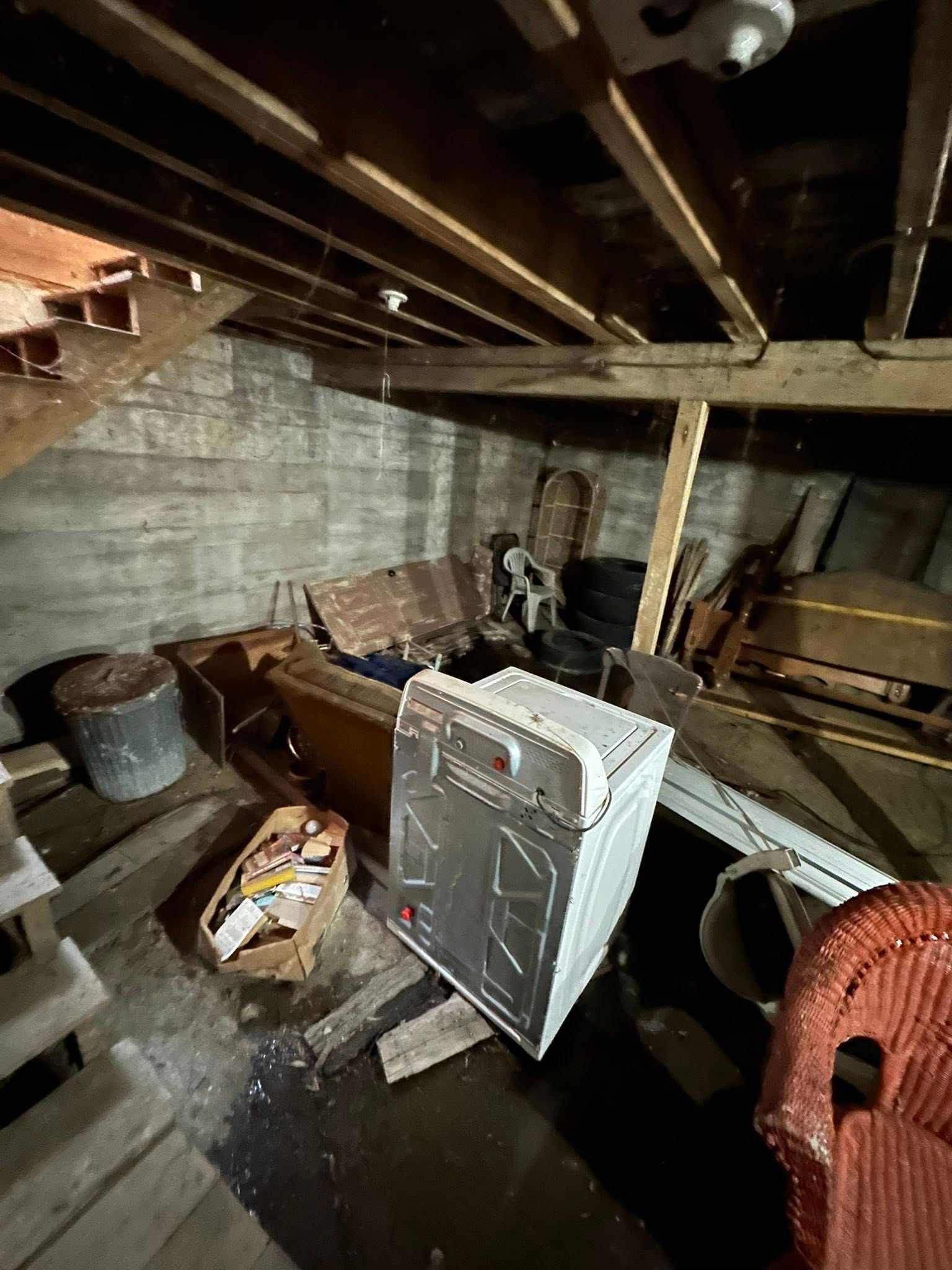 Cluttered basement with exposed beams, a portable heater, and scattered boxes and tools.