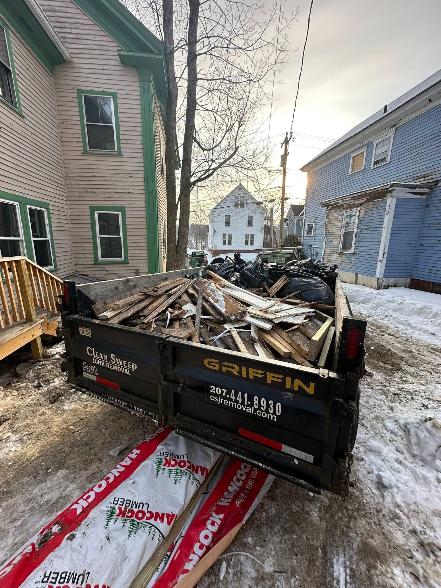 Dumpster full of demolition debris in a snowy alley between houses