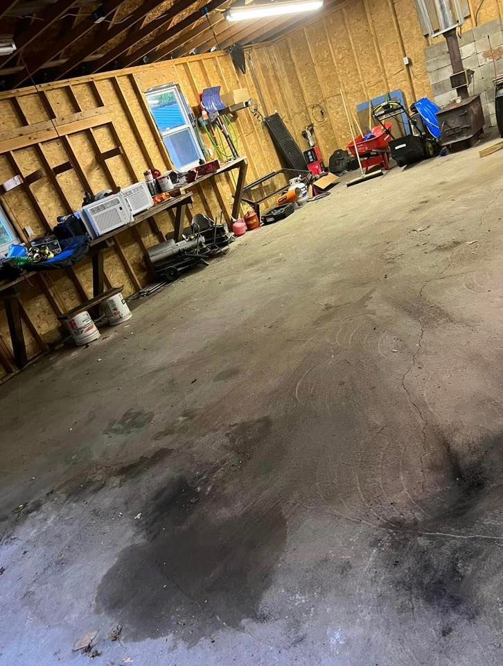 Empty garage with tools and equipment along the walls, and a wet stain on the concrete floor.