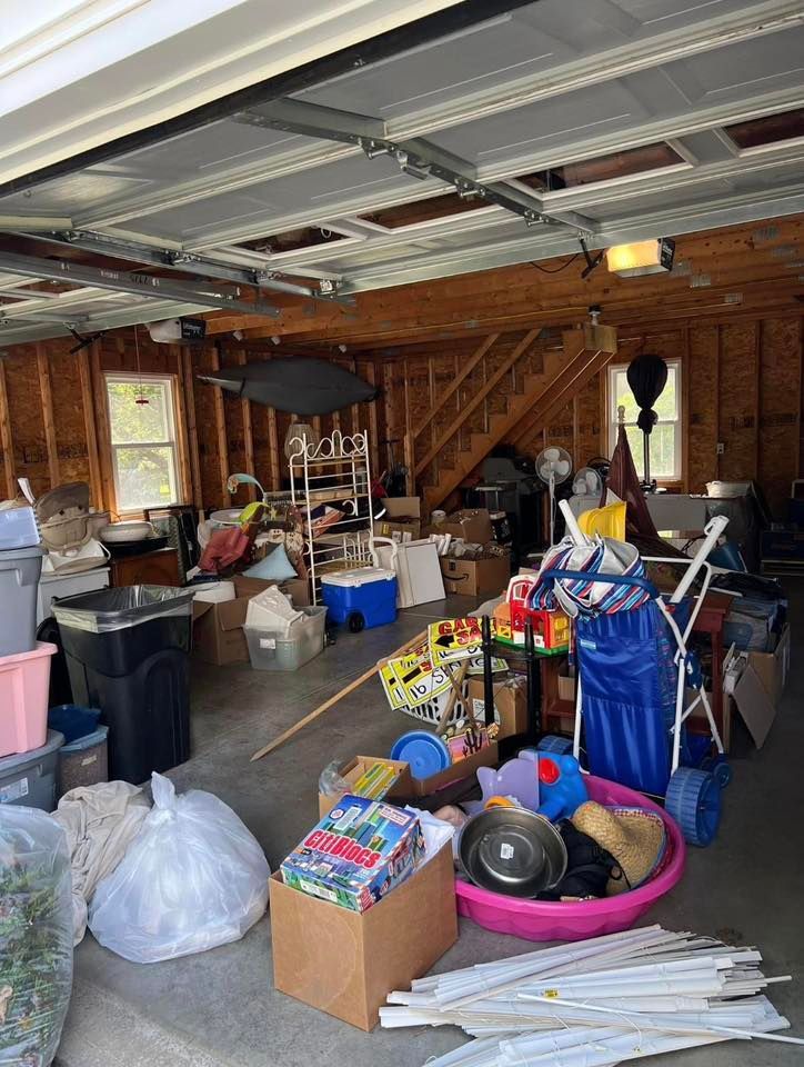 Cluttered garage with bins, boxes, tools, and a pink laundry basket under an open door.