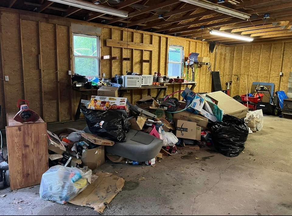 Cluttered garage interior with piles of trash bags, boxes, and debris scattered on the floor.