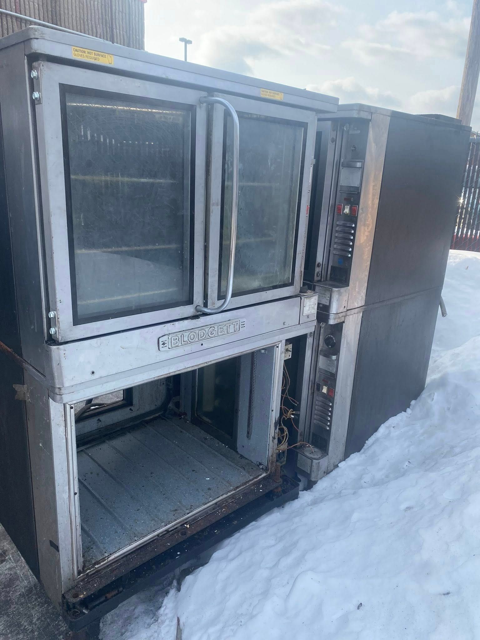 Open refrigerator on snowy ground with glass doors and shelves visible, outdoors in winter.