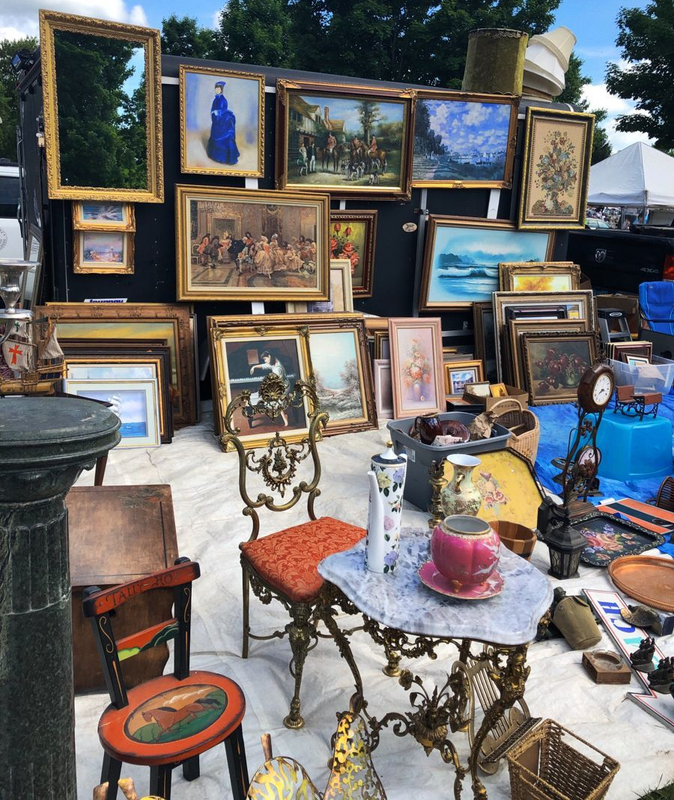 Outdoor flea market stall filled with framed paintings, mirrors, and antique furniture