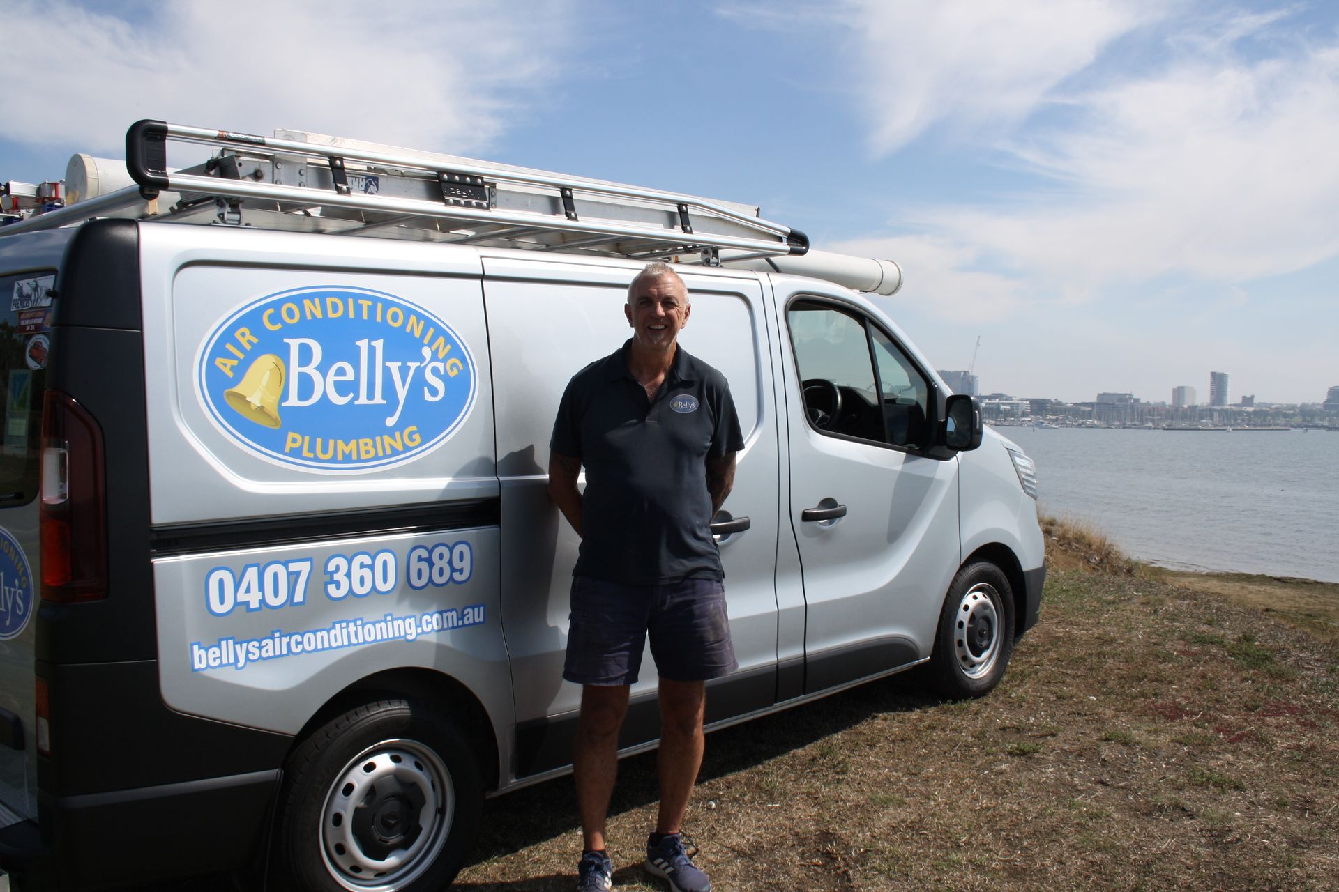 A technician in uniform standing in front of a Belly's Air Conditioning work vehicle. 