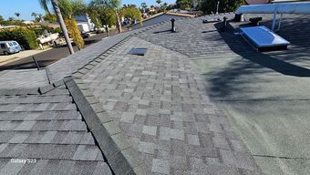 Overhead view of a gray shingled roof with a skylight and vents; houses and street in background.