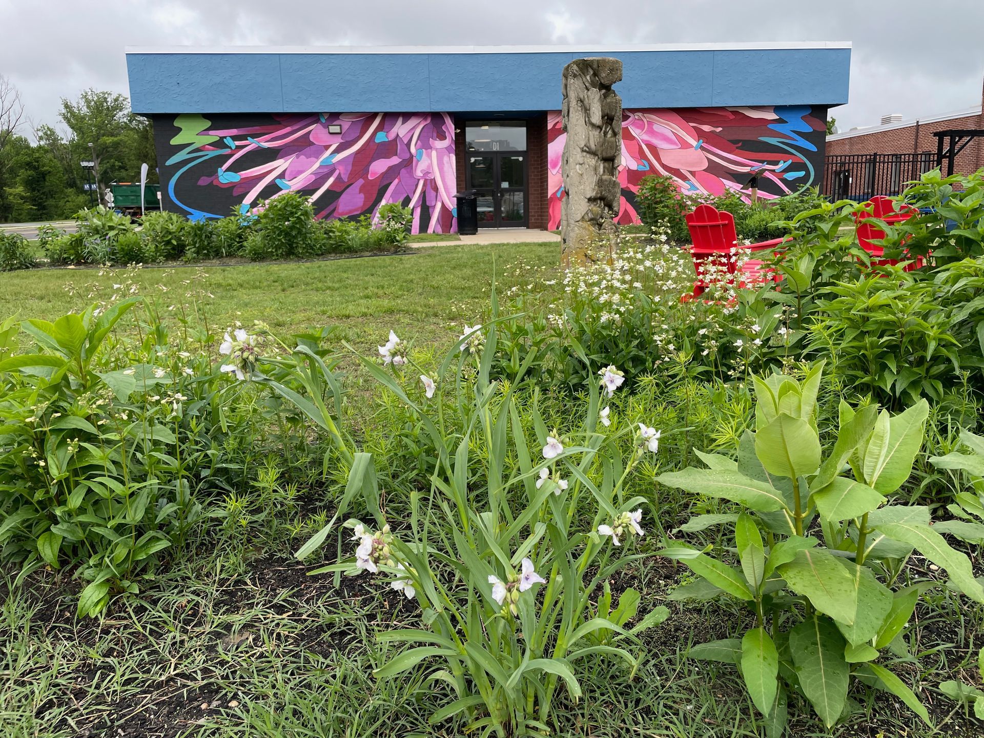 A large, vibrant floral mural covers the side of a white building in a parking lot, featuring colorful, oversized blooms.