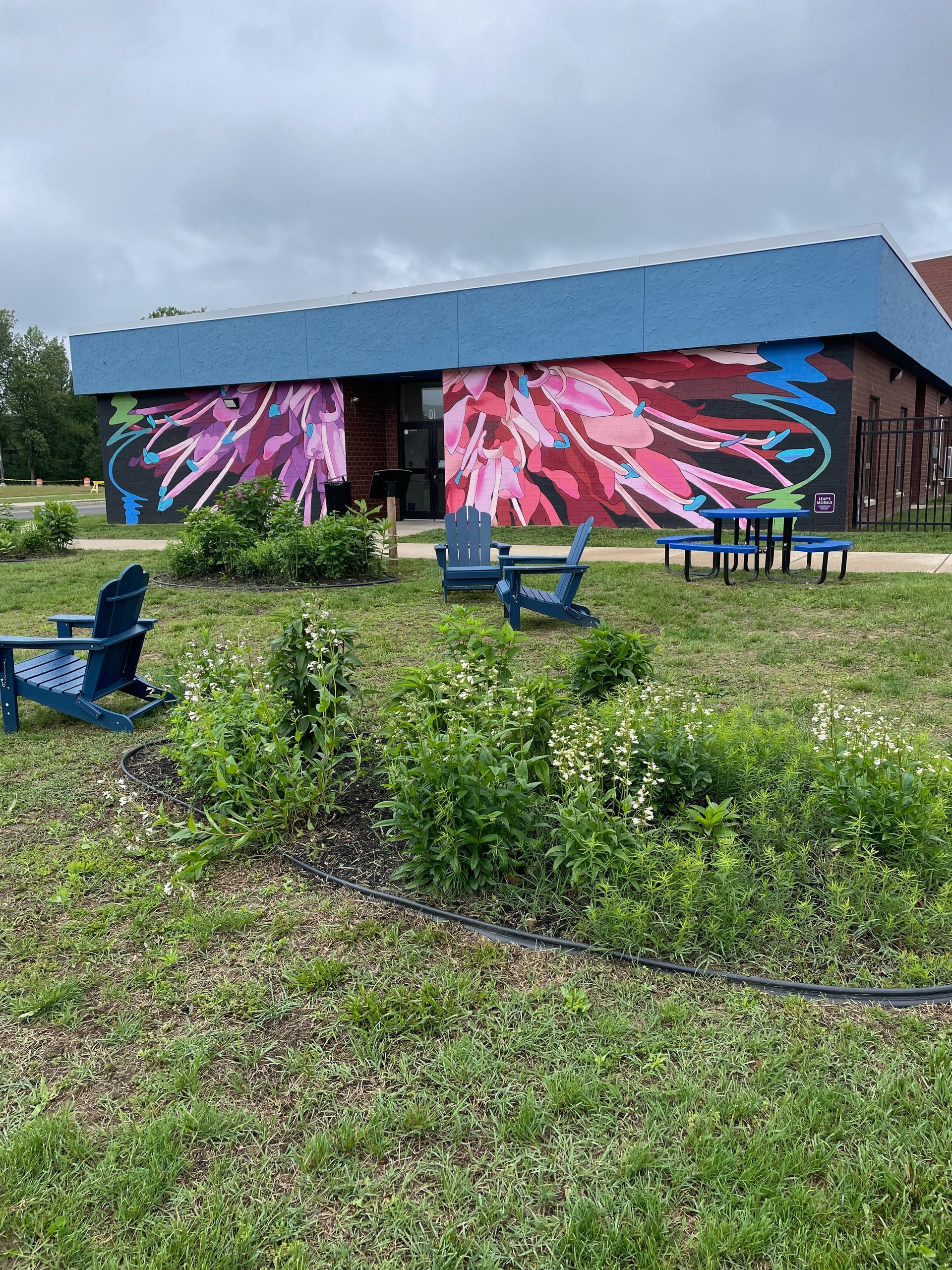 A colorful floral mural painted on the white side of a building above a parking lot.