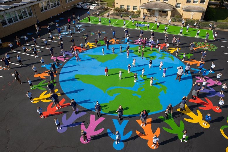 Students stand on a large painted map of the Earth on a playground, surrounded by a ring of colorful painted figures.