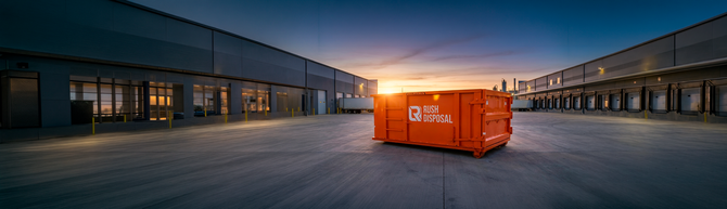 Orange shipping container in a warehouse yard at sunset, flanked by industrial buildings.