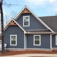 Blue-gray house with white trim and steep gables on a bare, wintery lot